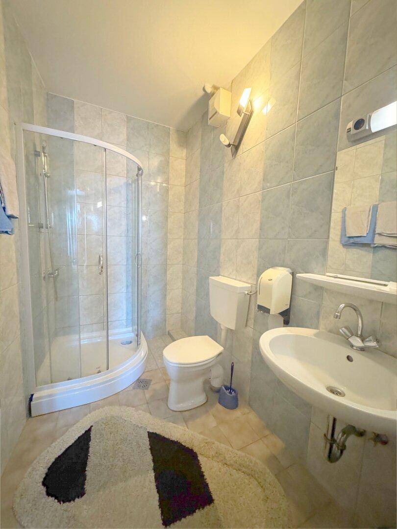 Badezimmer mit Duschkabine, WC und Waschbecken, gefliest in hellblauen und weißen Streifen.