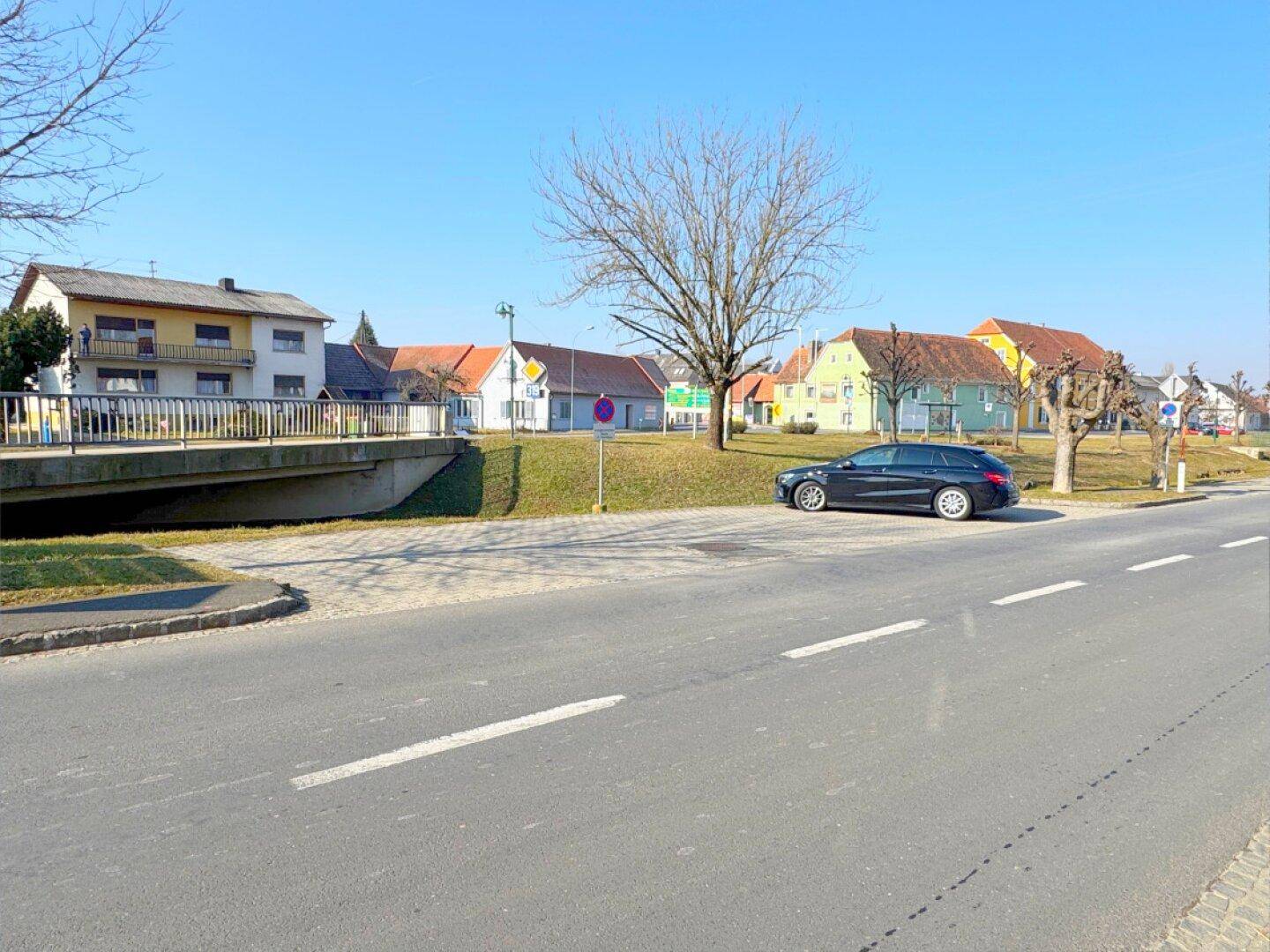 Ländliche Straßenansicht mit Wohnhäusern, Brücke und geparktem Auto.