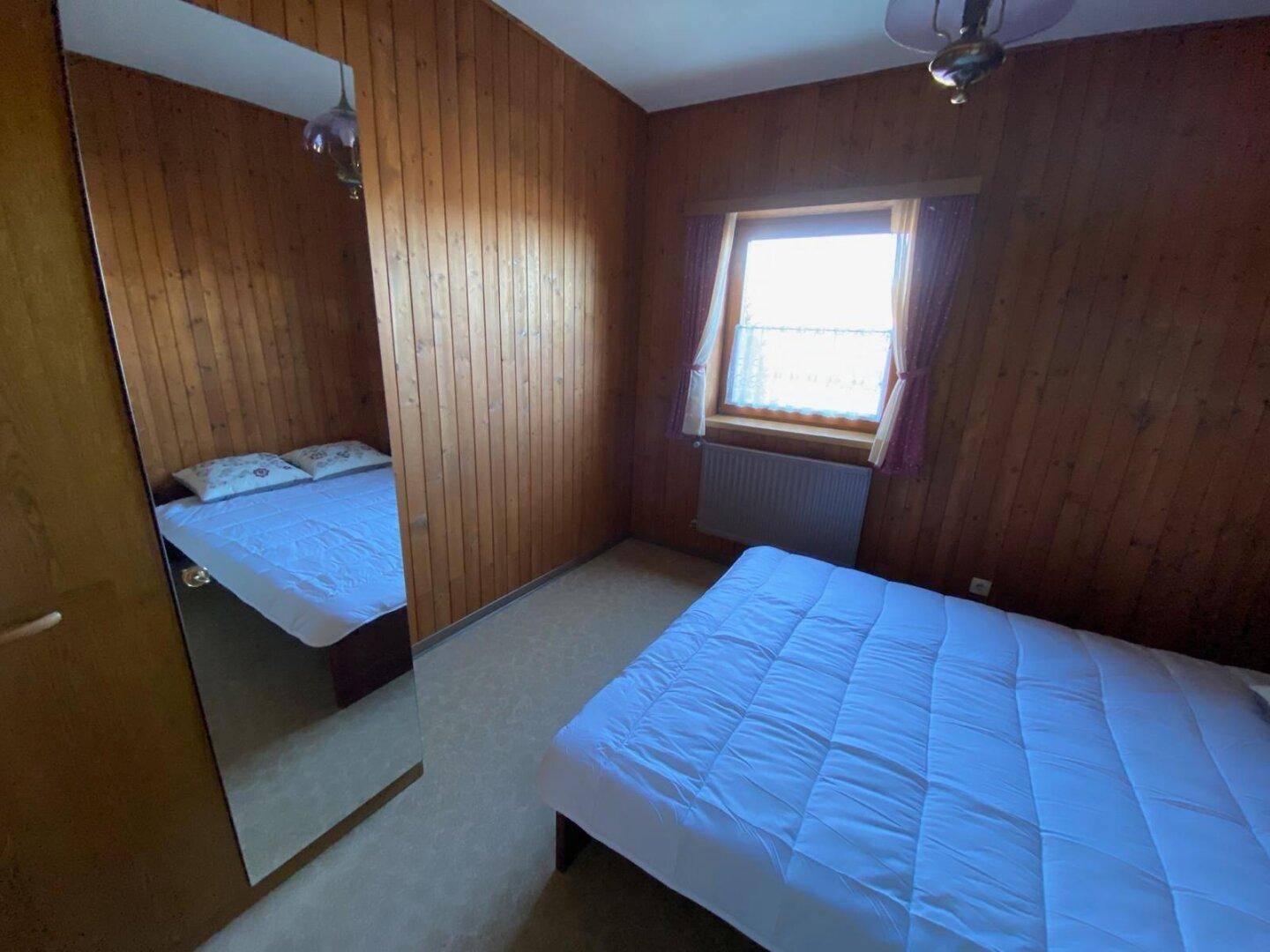 Schlafzimmer mit Vinylboden, Holzvertäfelung und Doppelbett, inklusive großem Spiegelschrank.