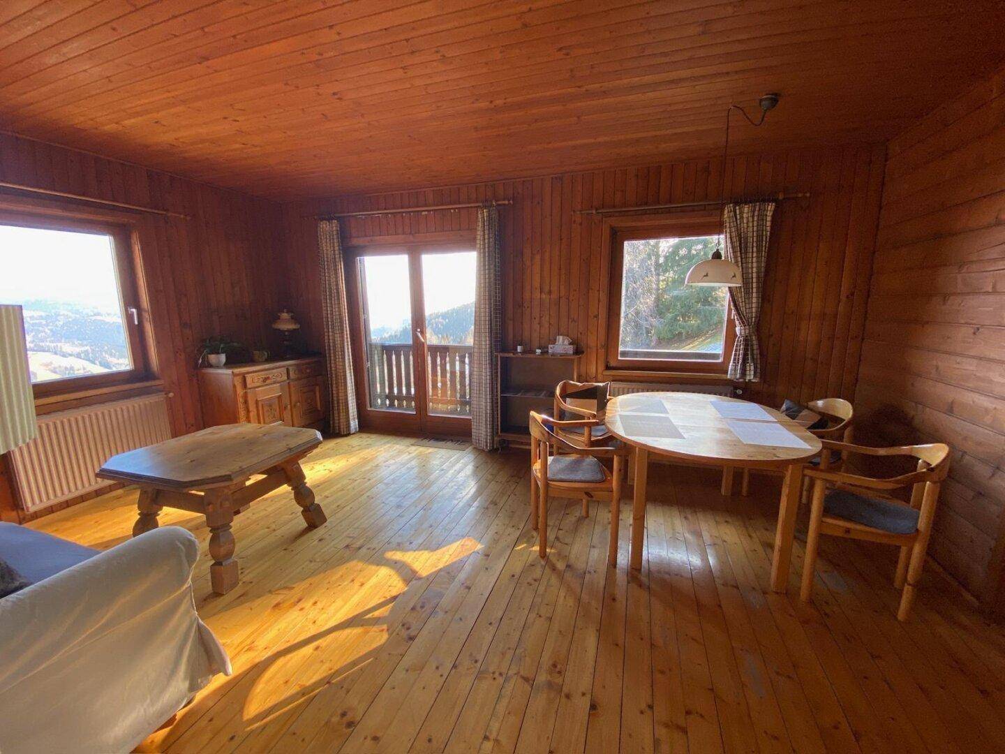 Gemütlicher Wohn-Essbereich mit viel Holz, Parkettboden und Zugang zum Balkon mit Bergblick.