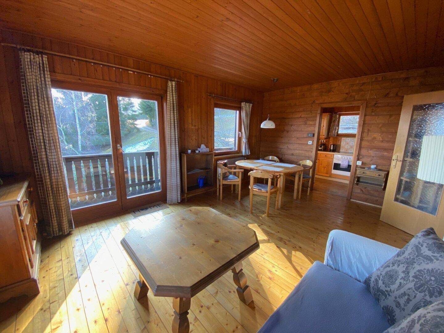 Heller Wohn-Essbereich mit Holzboden, Holzvertäfelung und Blick ins Grüne sowie Zugang zum Balkon.