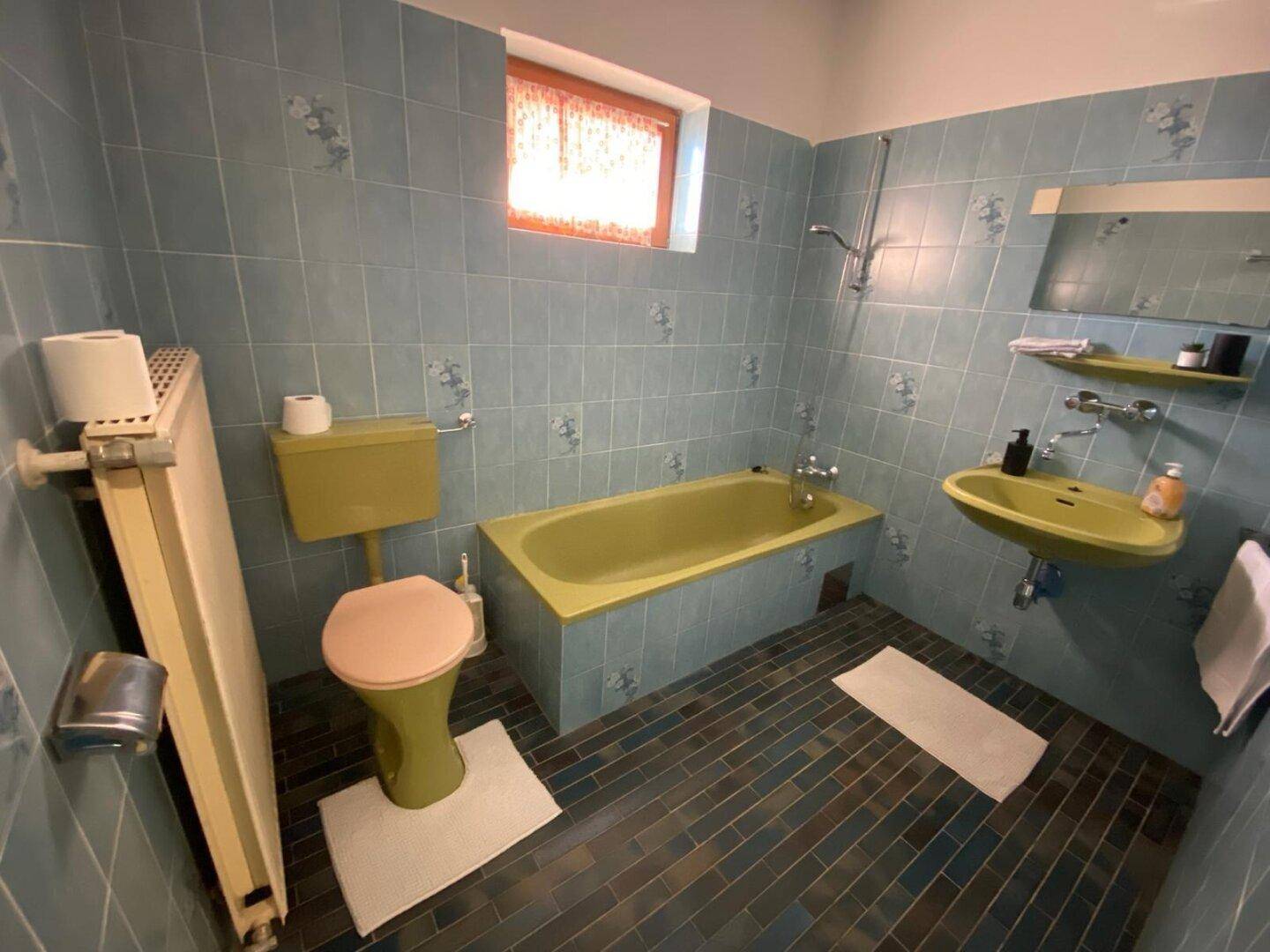 Badezimmer im Stil der 80er Jahre mit blauen Fliesen, grüner Badewanne und passendem WC.