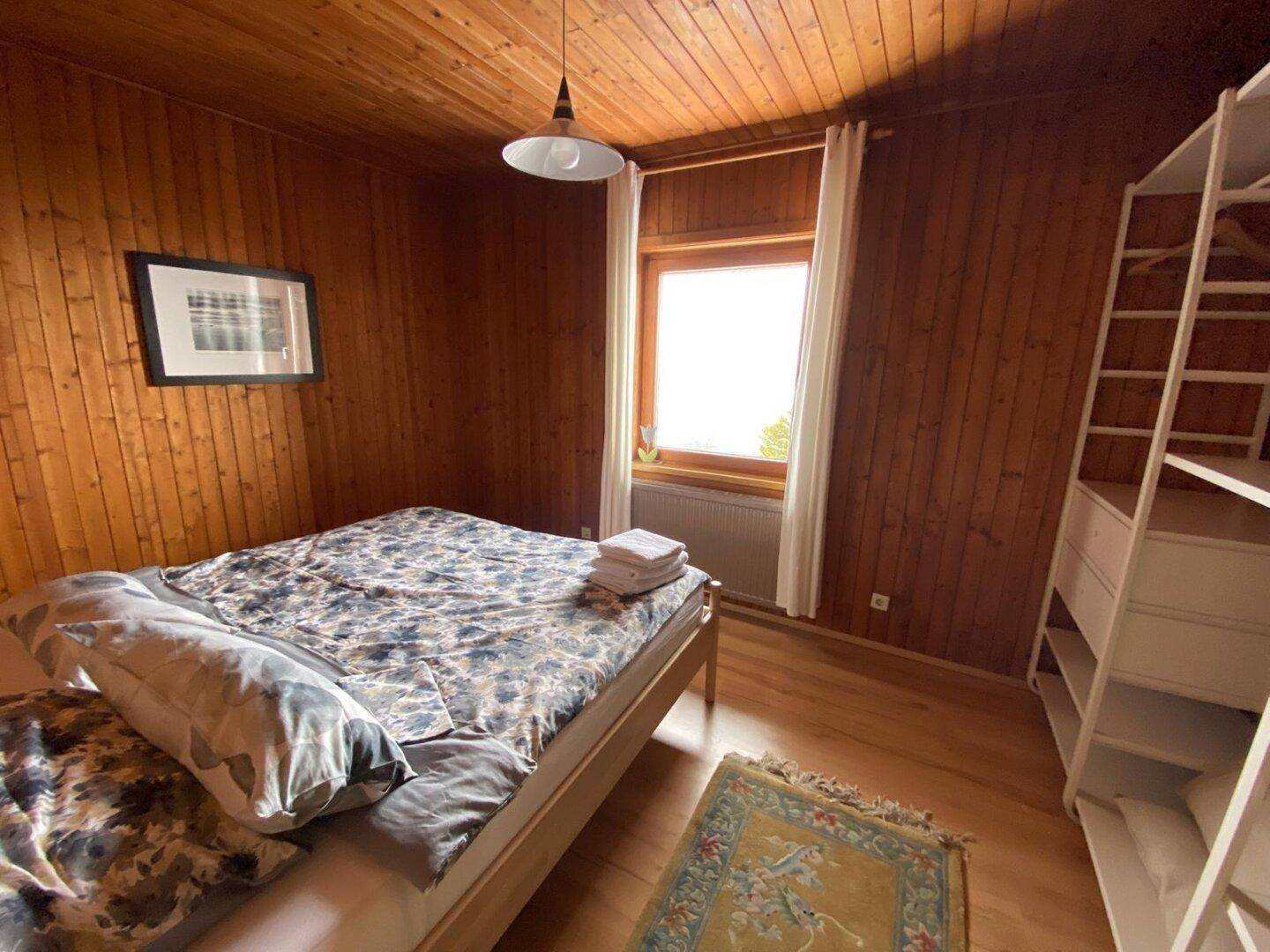 Schlafzimmer mit Holzboden, Holzvertäfelung und Doppelbett, ausgestattet mit einem offenen Kleiderschrank.