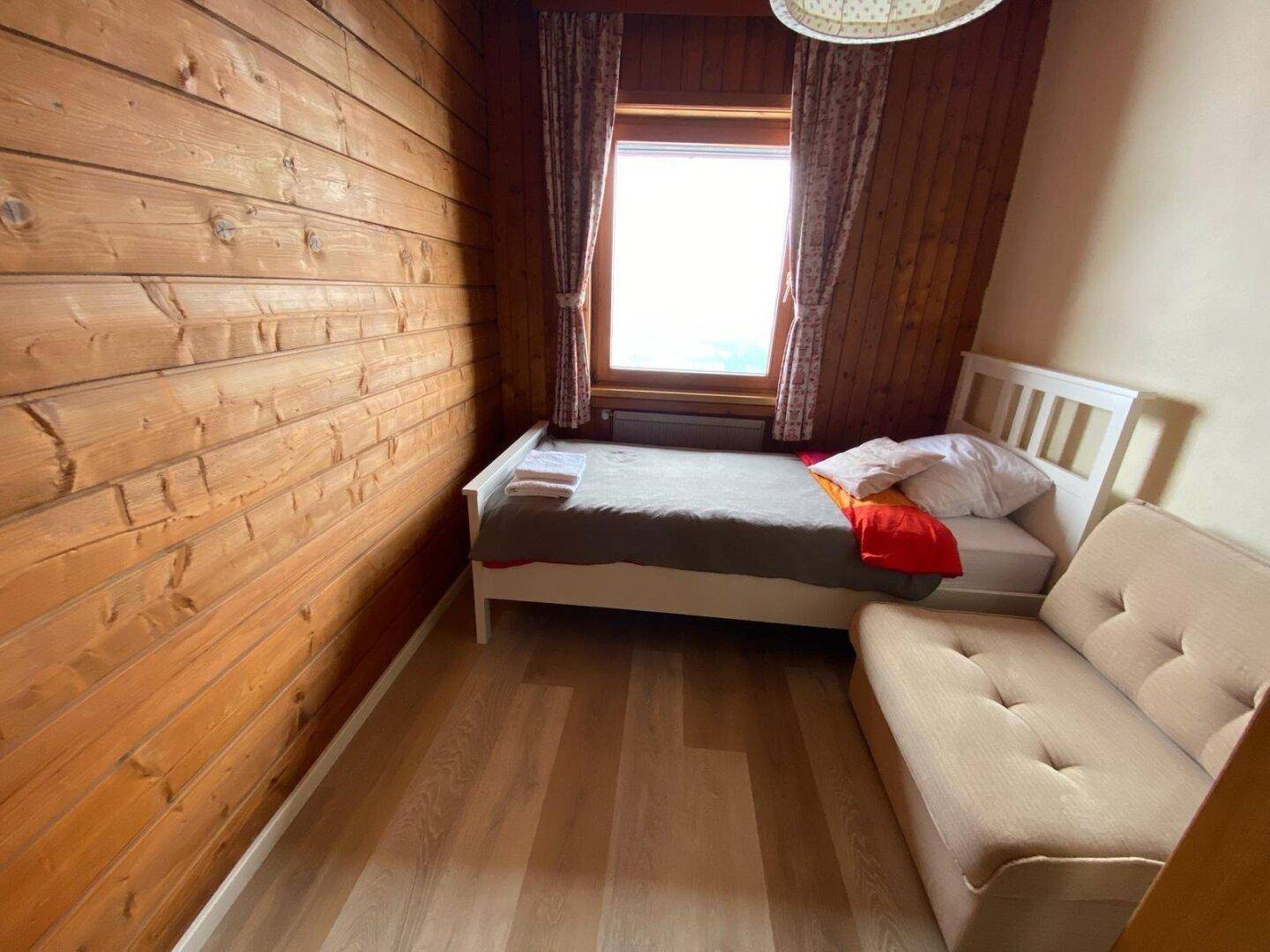 Kleines Schlafzimmer mit Holzwänden, Einzelbett und einem Sofa, ideal als Kinder- oder Gästezimmer.