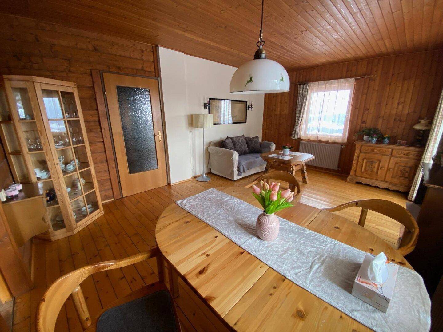Rustikaler Wohn-Essbereich mit Holzboden und Holzvertäfelung, gemütlicher Sitzecke und Blick nach draußen.