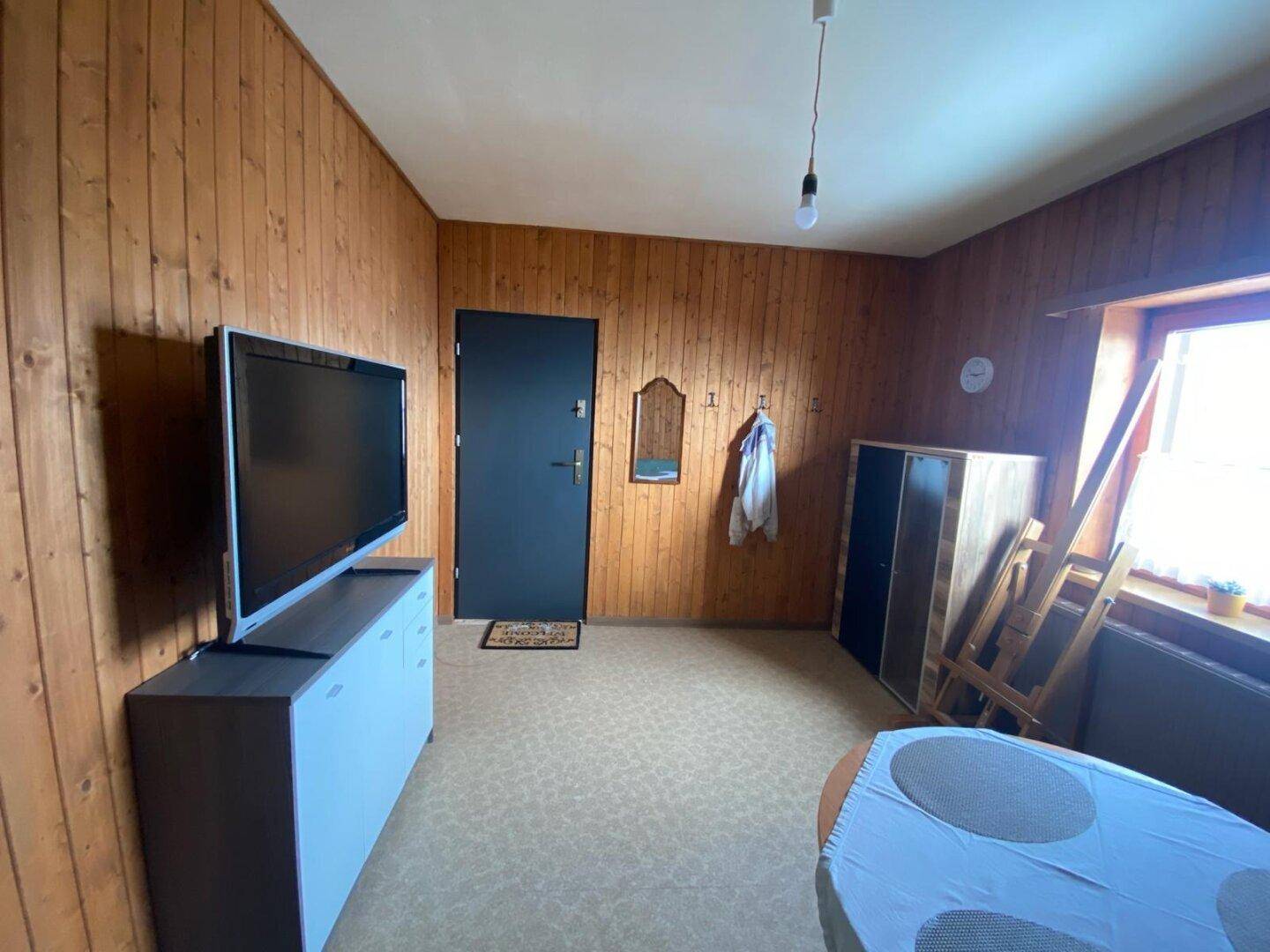 Wohnbereich mit Holzwänden, Fernseher und einem Tisch, der als Ablage dient.