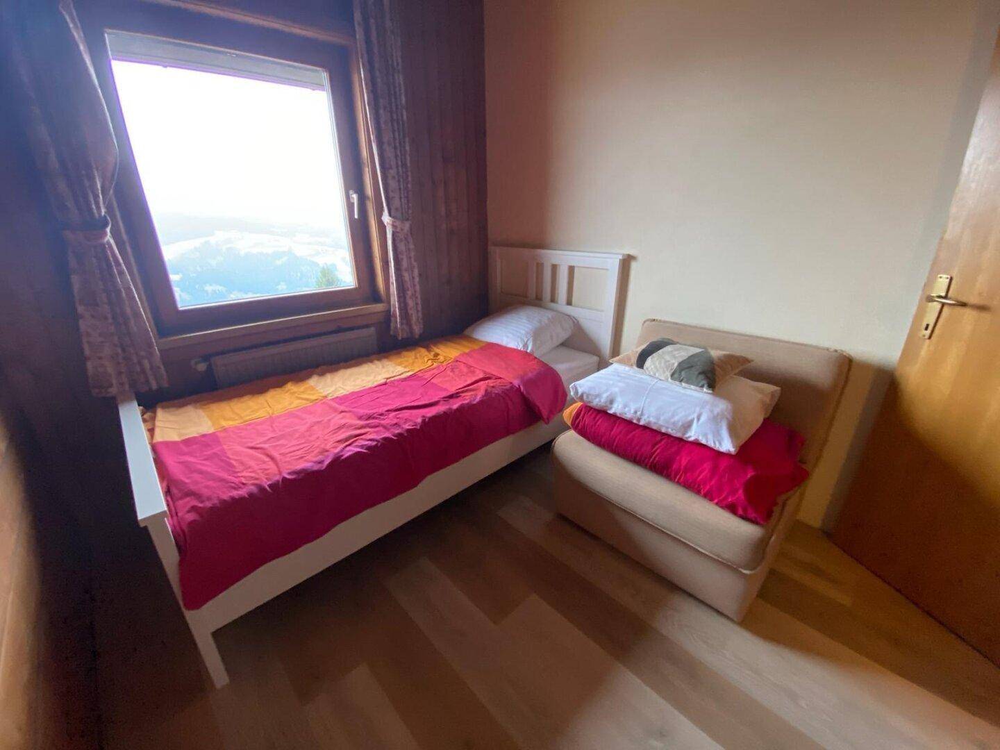 Helles Schlafzimmer mit Holzboden, Einzelbett und einem Sessel, ideal als Gästezimmer.
