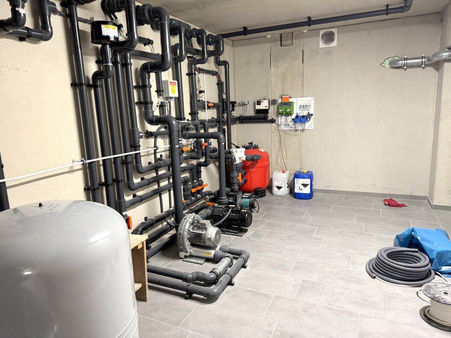 Technikraum mit komplexen Rohrleitungssystemen und Pumpen im Untergeschoss.
