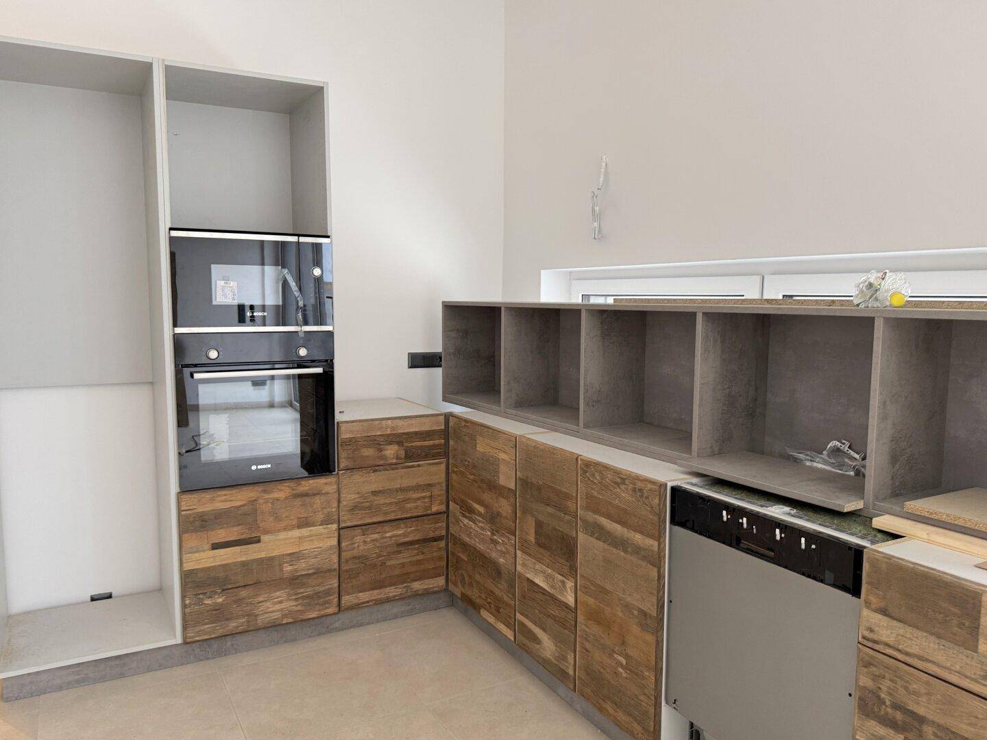 Küche im Bau mit Holzelementen, Einbauofen und Geschirrspüler.