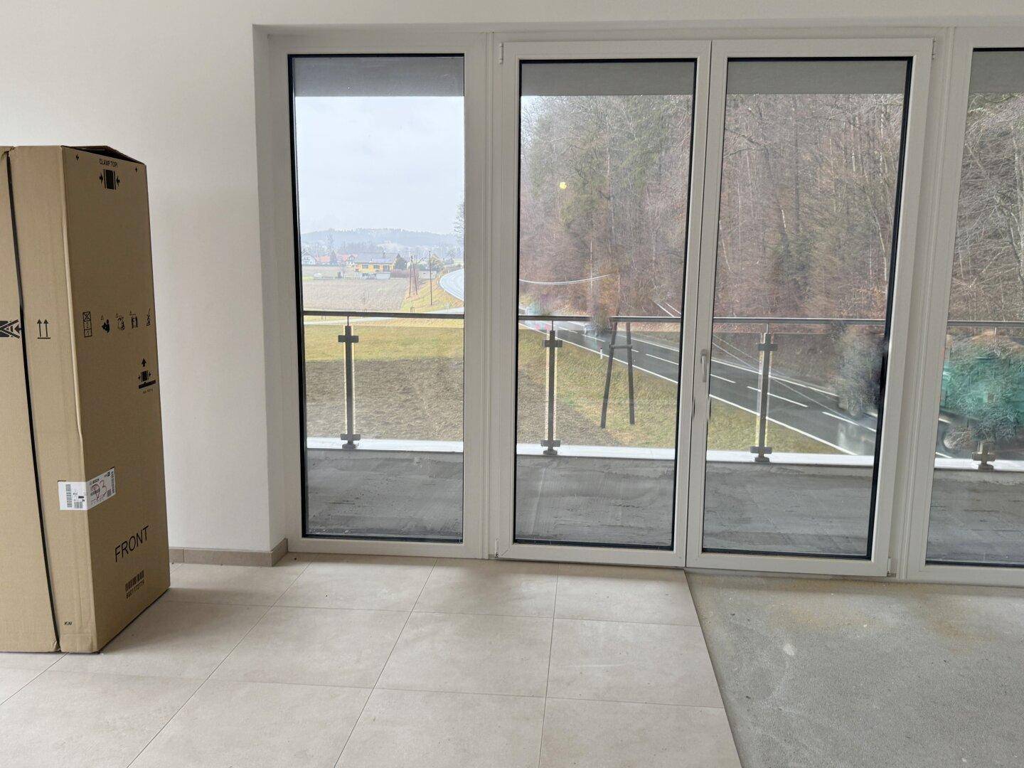 Heller Raum mit großen Fenstern und Balkonzugang, Blick auf die Landschaft.