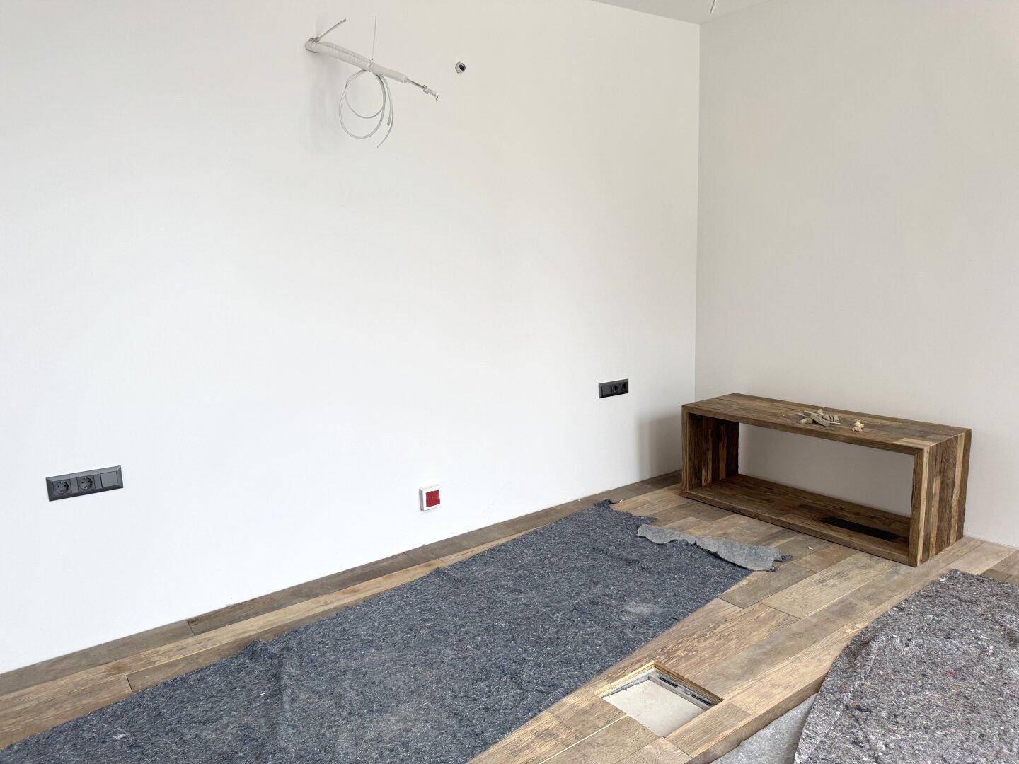 Helles Zimmer mit Holzboden und eingebauter Holzbank, bereit für die Einrichtung.