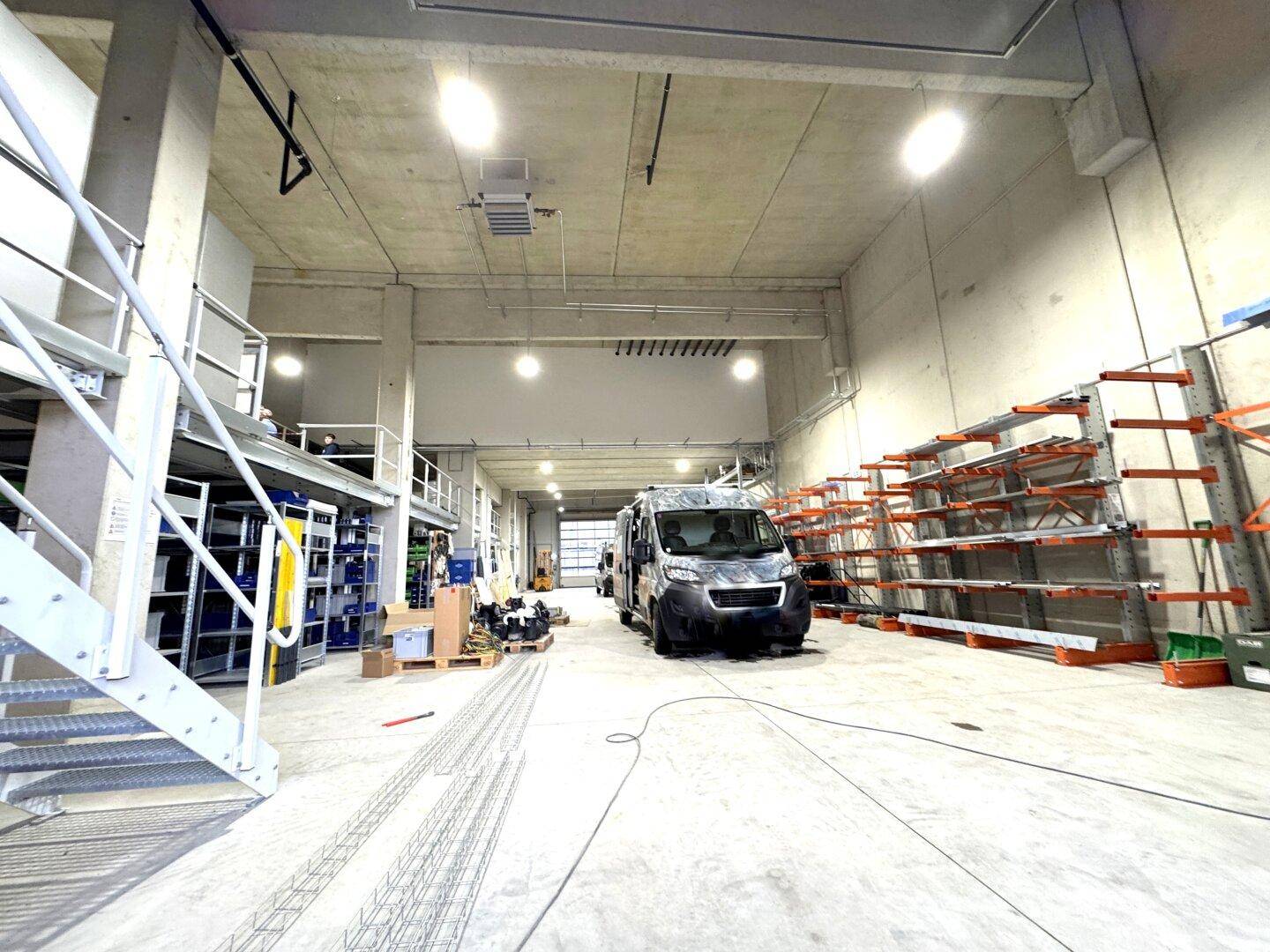 Große Lagerhalle oder Garage mit hohen Decken und Betonboden, ein Fahrzeug ist geparkt.