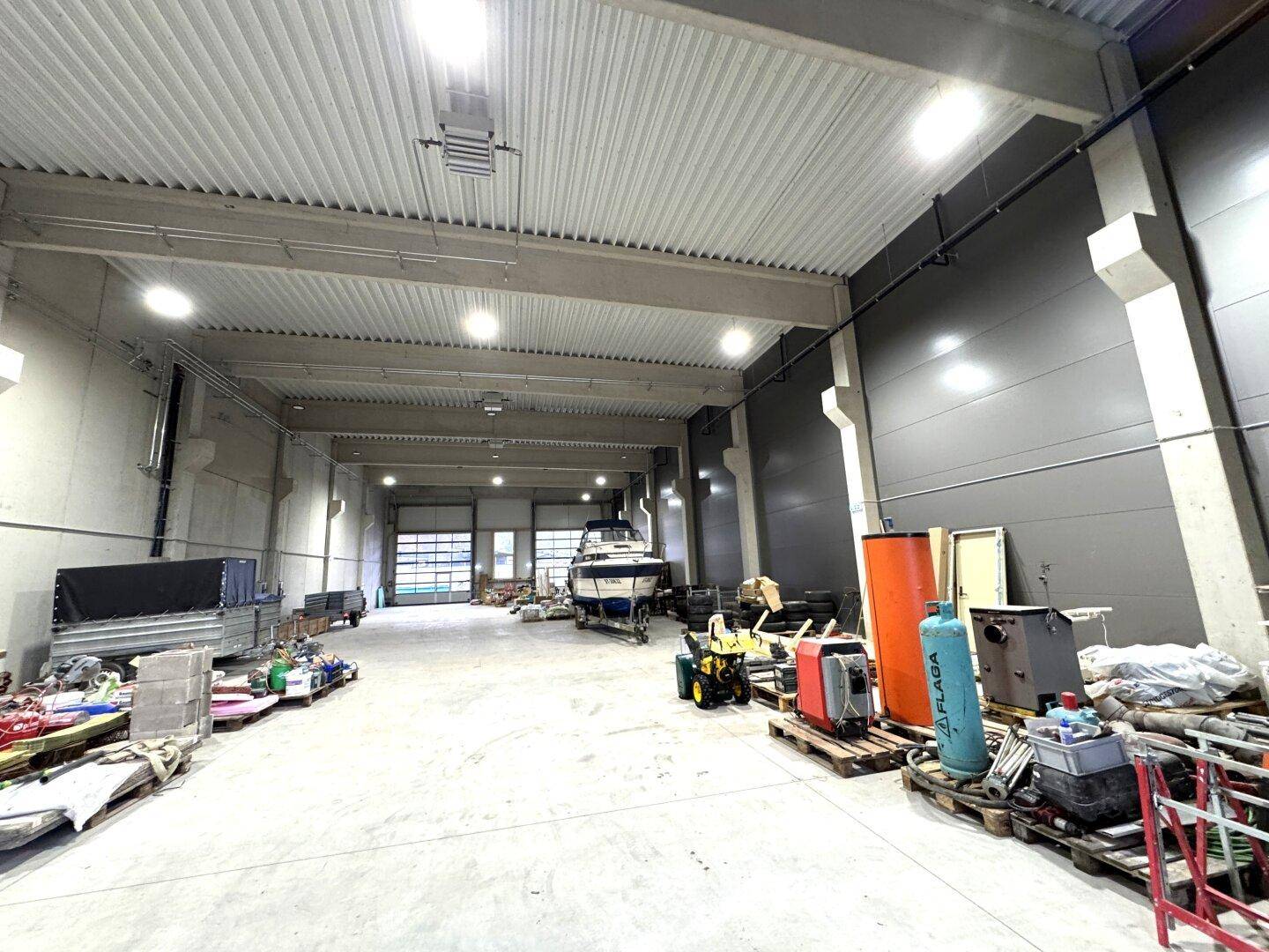 Geräumige Lagerhalle mit hohen Decken, Rolltoren und einem Boot auf einem Anhänger.