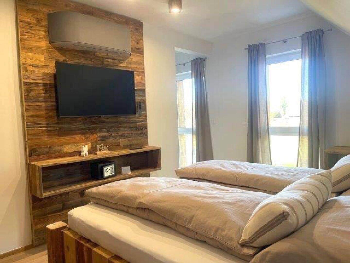 Gemütliches Schlafzimmer mit Holzwand, Fernseher und Zugang zum Balkon.