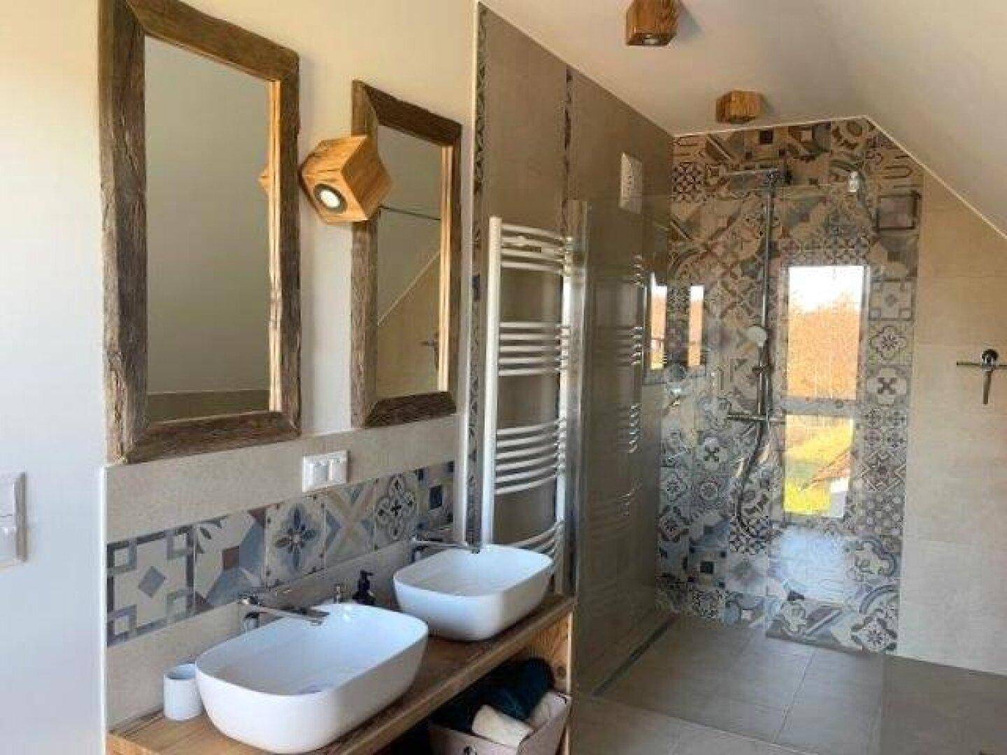 Modernes Badezimmer mit Doppelwaschbecken, begehbarer Dusche und gemusterten Fliesen.
