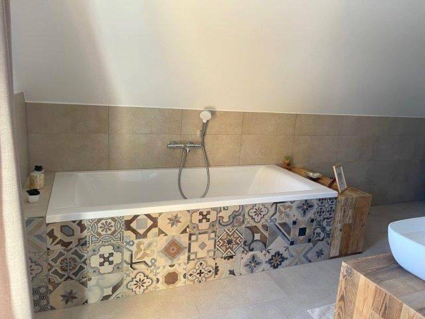 Badewanne mit gemusterten Fliesen und Holzelementen in einem hellen Badezimmer.