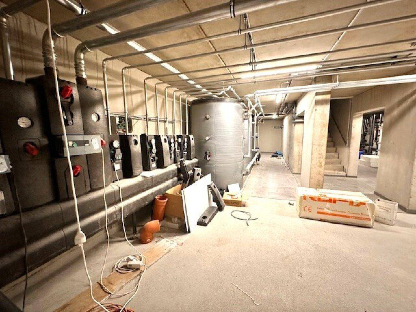 Technikraum im Keller mit Heizungsanlagen und Rohrleitungen.