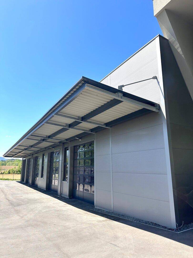 Moderne Gebäudefassade mit großen Garagentoren und Vordach unter blauem Himmel.