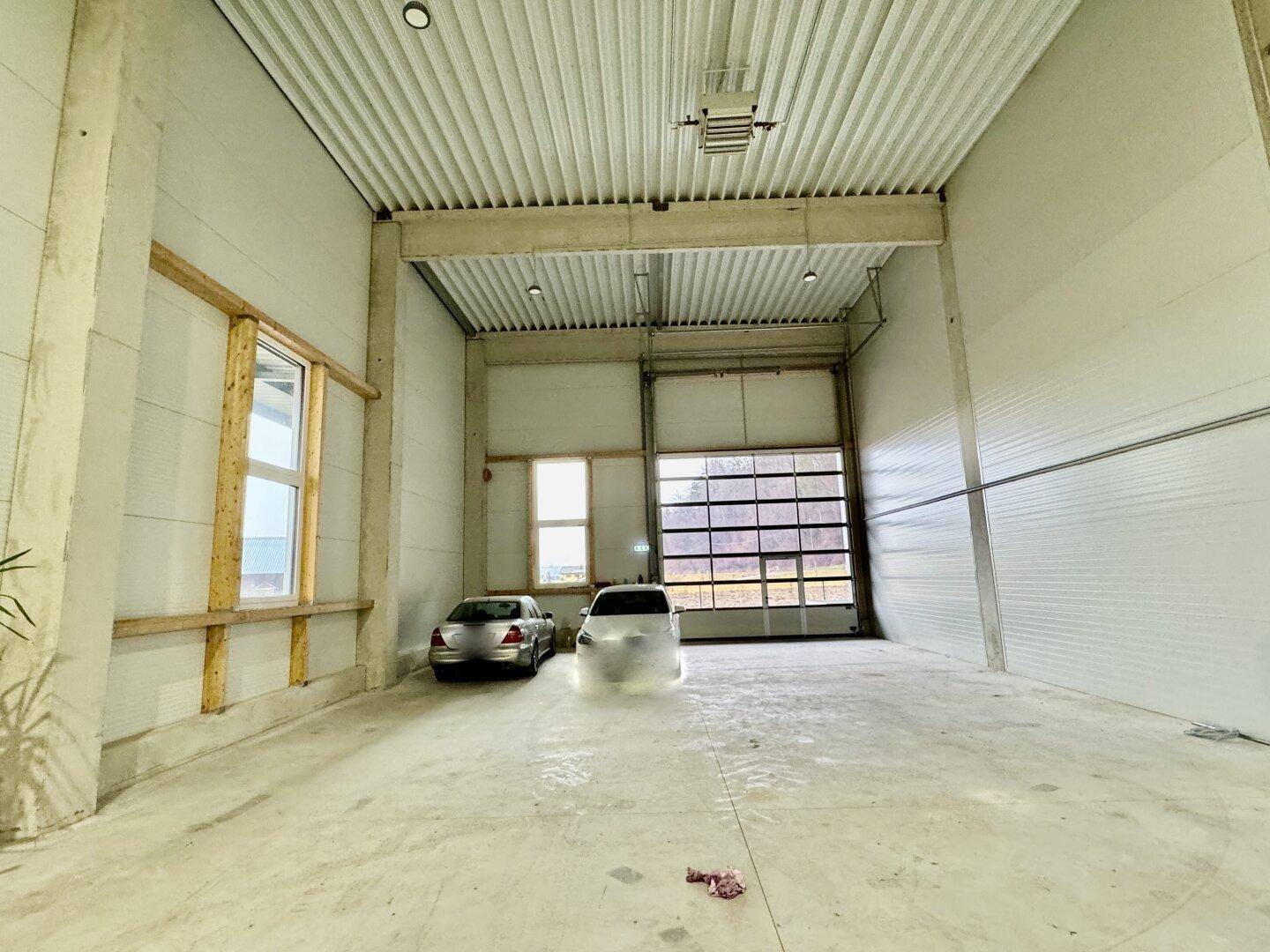 Geräumige Garage mit hohen Decken und Betonboden, zwei Fahrzeuge sind geparkt.