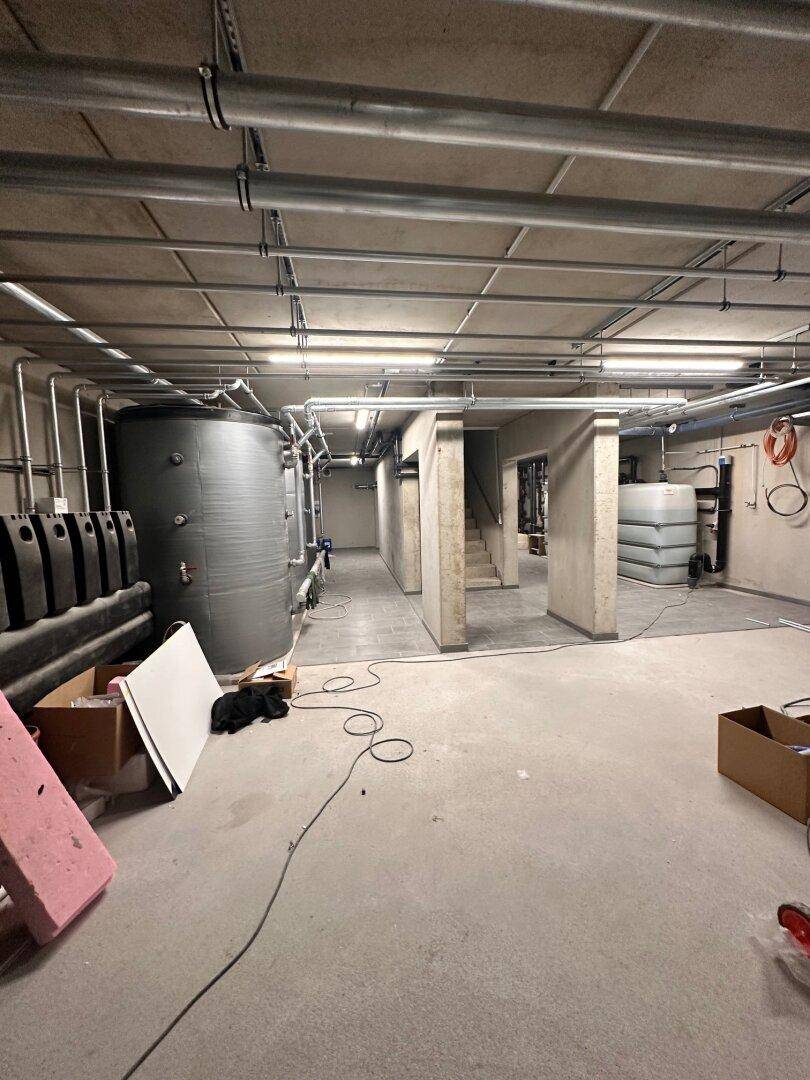 Technikraum im Keller mit Heizungsanlagen und Rohrleitungen.