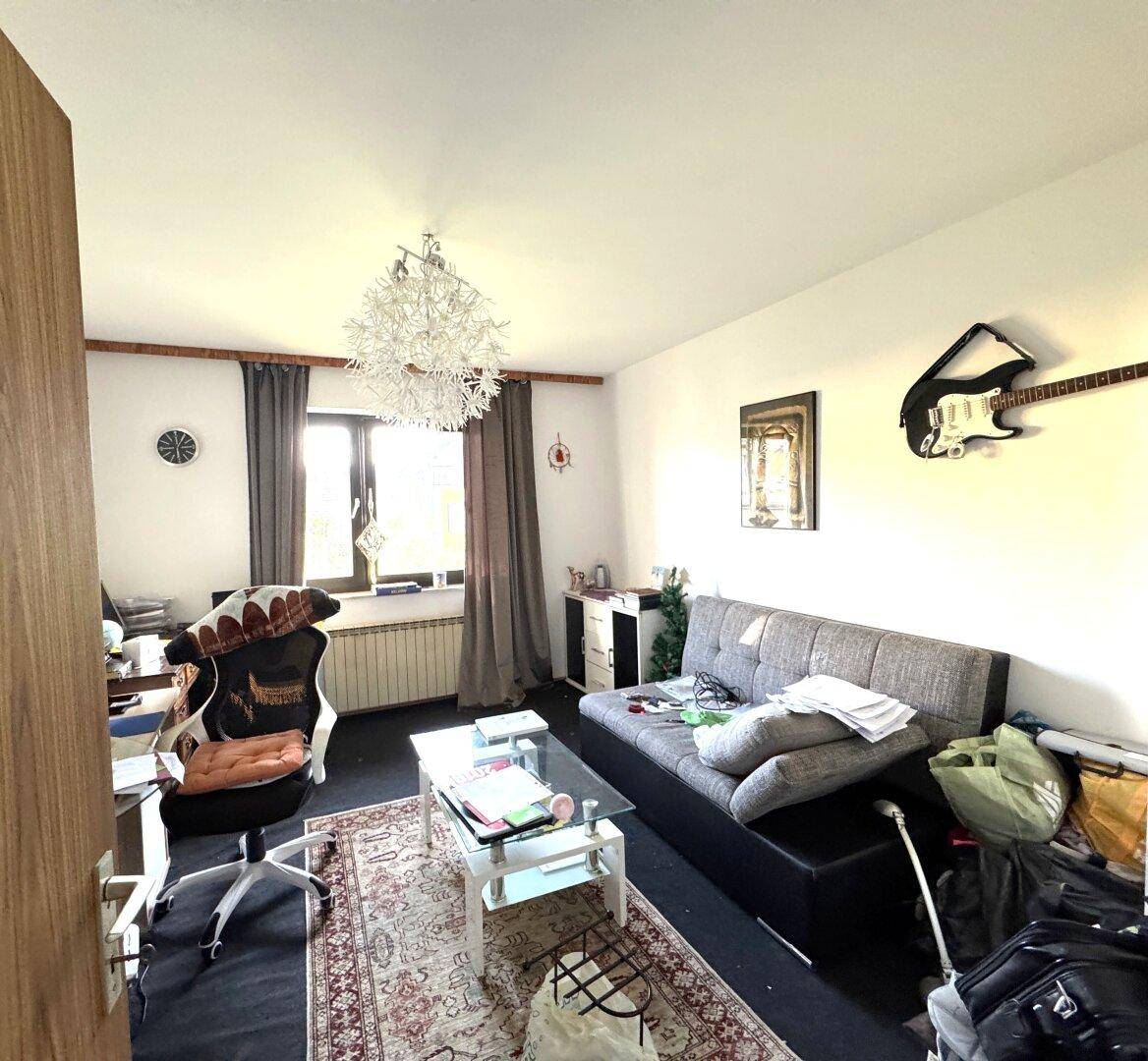 Wohnzimmer mit Sofa, Schreibtisch und Teppichboden, dekoriert mit einer Gitarre an der Wand.