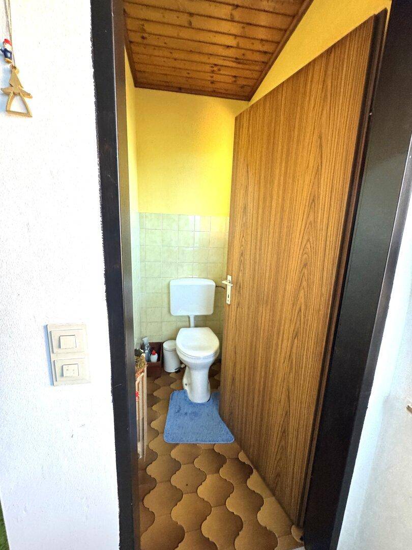 Kleines Gäste-WC mit gefliesten Wänden, WC und Holzdecke, in einem älteren Stil.
