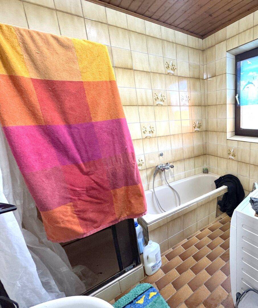 Badezimmer mit Badewanne, Fliesenboden und Fenster, ausgestattet mit einer Waschmaschine.