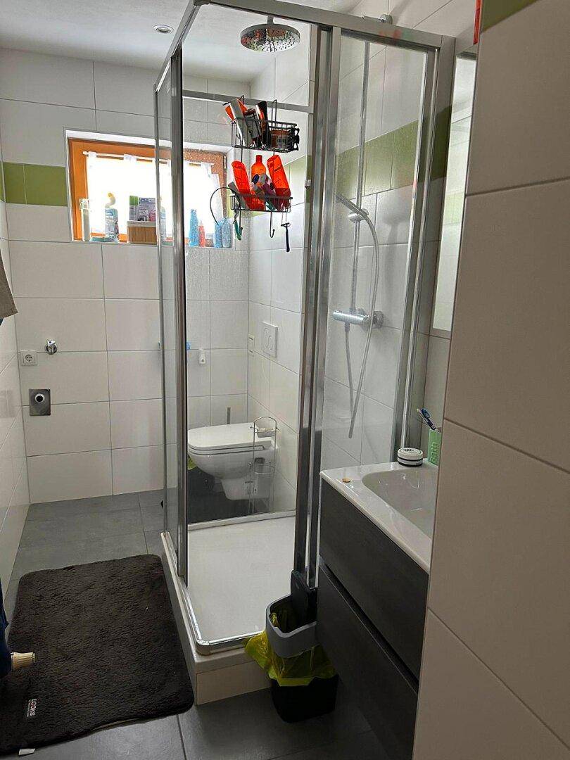Modernes Badezimmer mit Duschkabine, WC und Fenster für Tageslicht und Belüftung.
