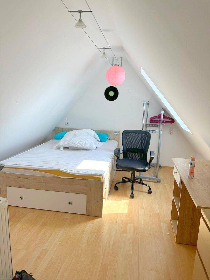 Schlafzimmer im Dachgeschoss mit Holzboden, Dachfenster und einfacher Einrichtung für viel Licht.