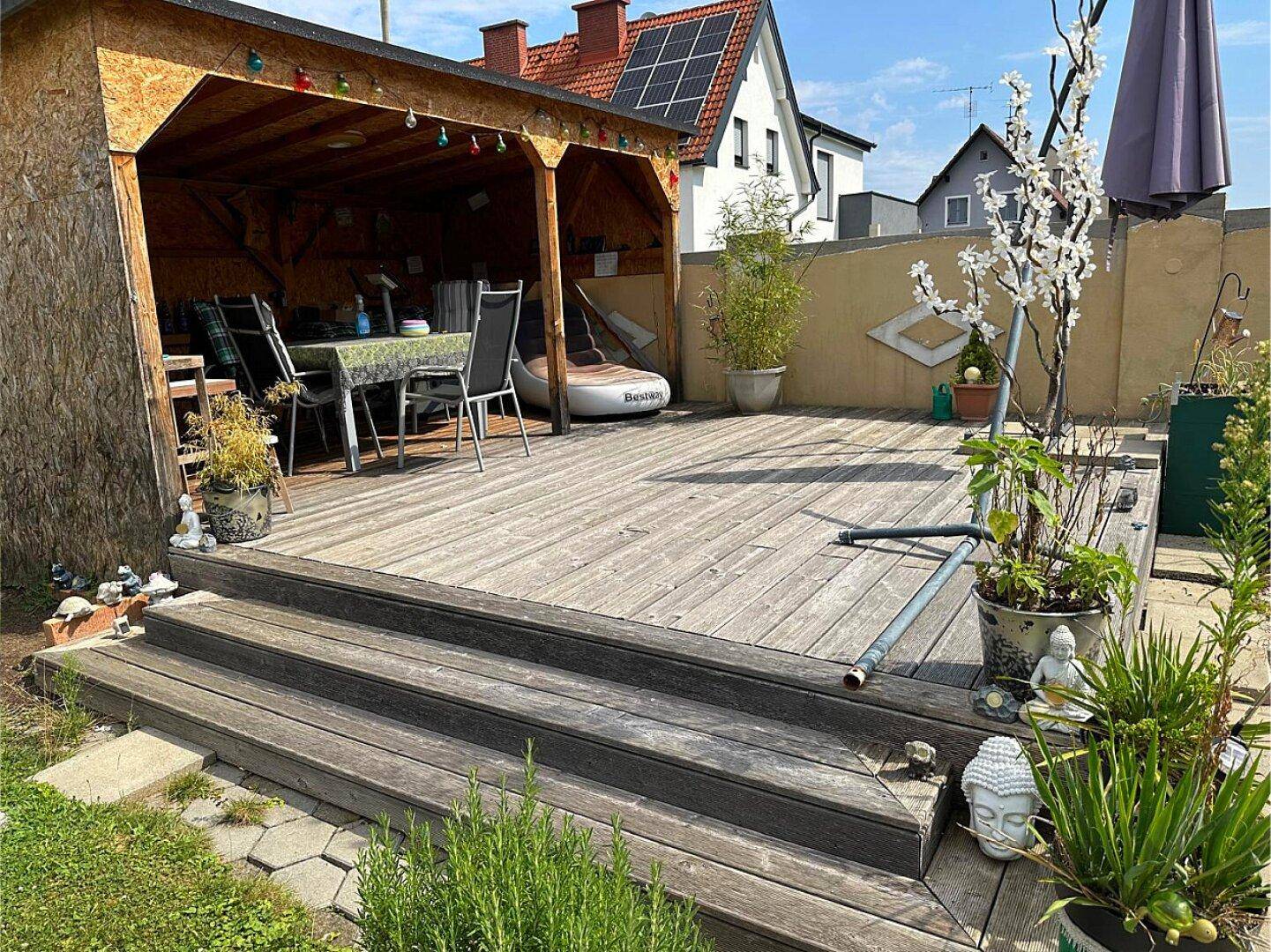 Geräumige Holzterrasse mit überdachtem Sitzbereich und Pflanzen in Töpfen für entspannte Stunden.