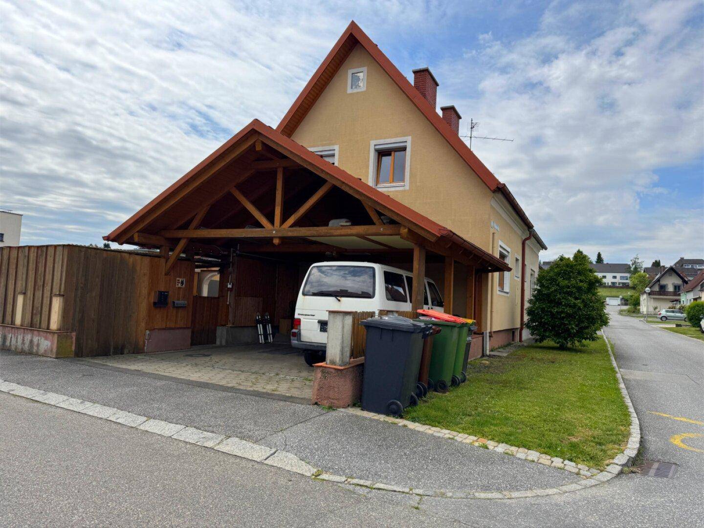 Freistehendes Einfamilienhaus mit überdachtem Carport und gepflegtem Vorgarten unter blauem Himmel.
