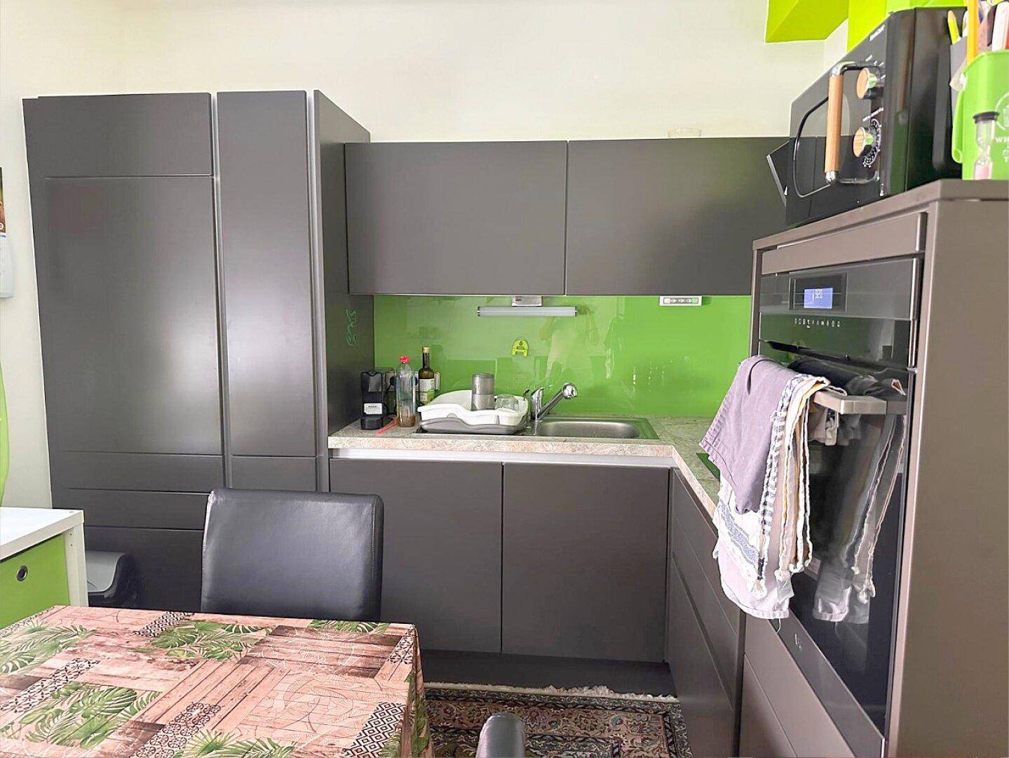 Moderne Küche mit grauen Fronten, grüner Rückwand und integrierten Geräten für effizientes Kochen.