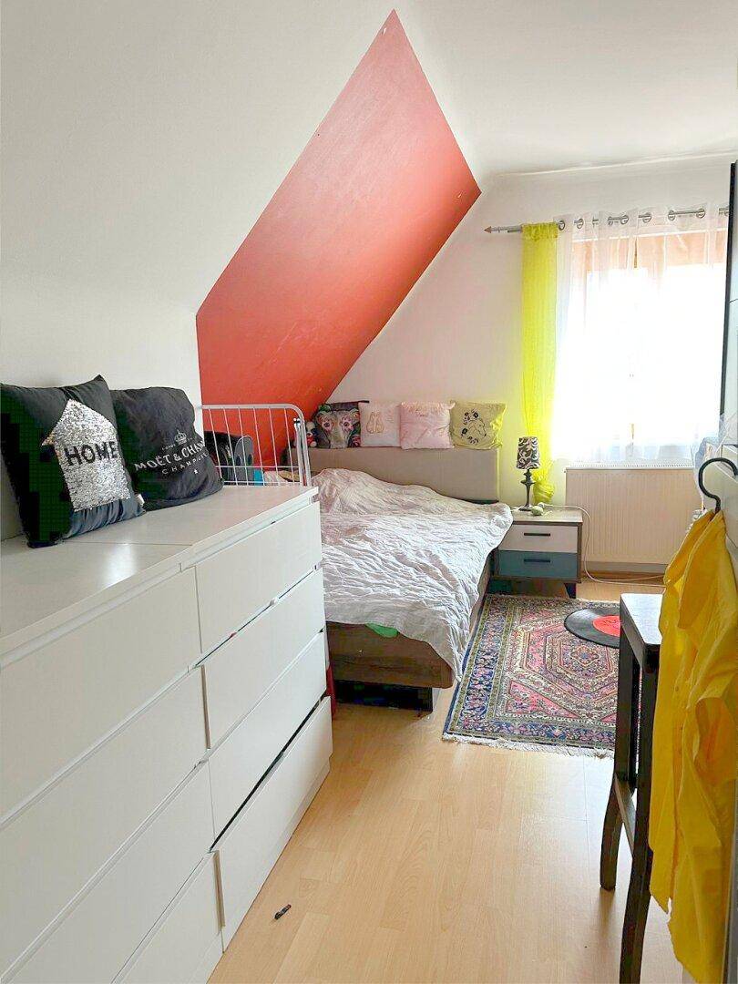 Schlafzimmer mit Dachschräge, Holzboden und farbiger Wandgestaltung für individuellen Charme.
