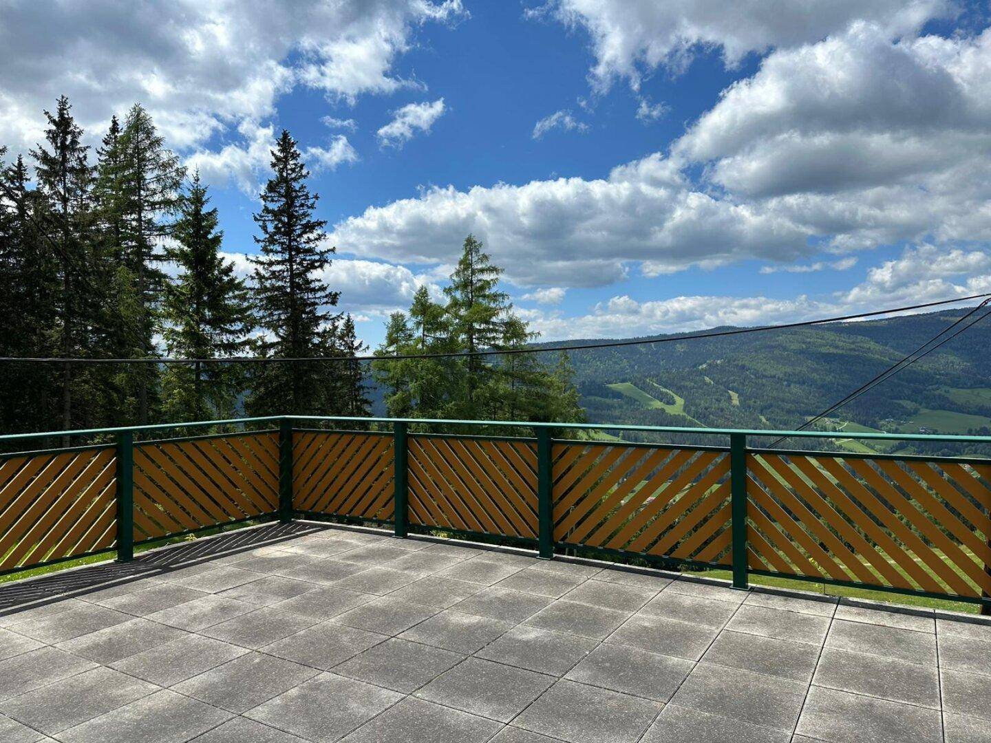Große geflieste Terrasse mit Holzgeländer und weitem Blick auf die grüne Berglandschaft.