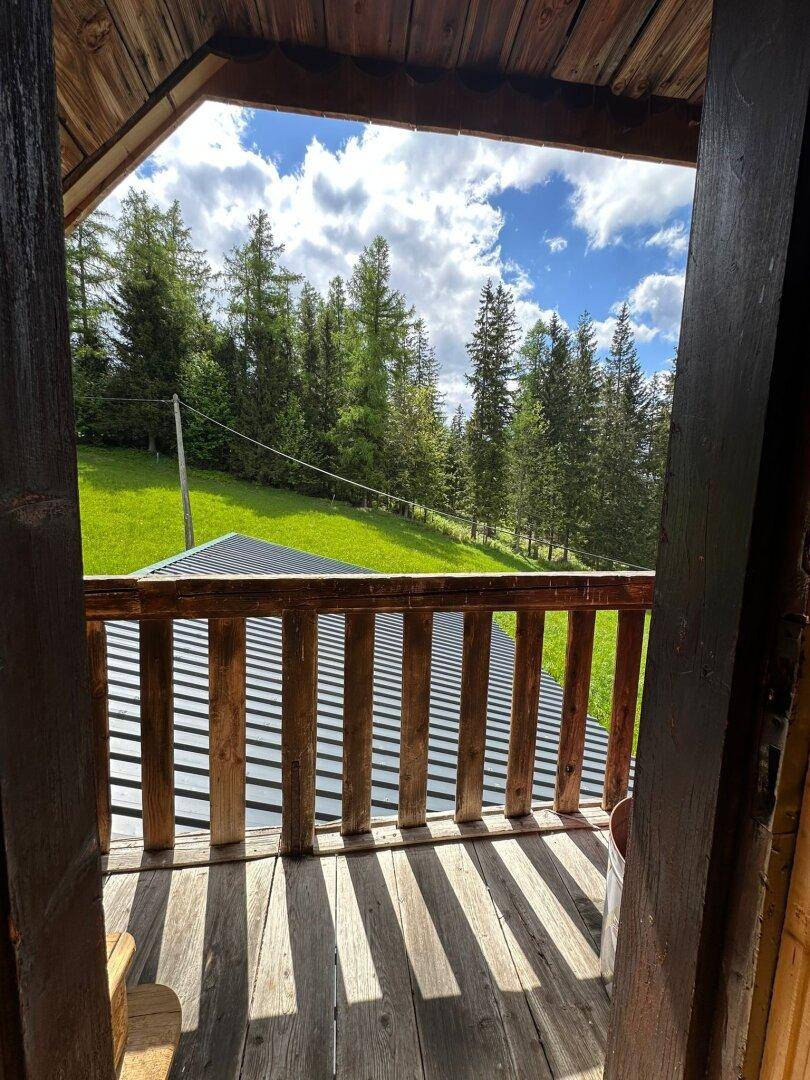 Rustikaler Holzbalkon mit Blick auf die umliegenden grünen Wälder und den blauen Himmel.