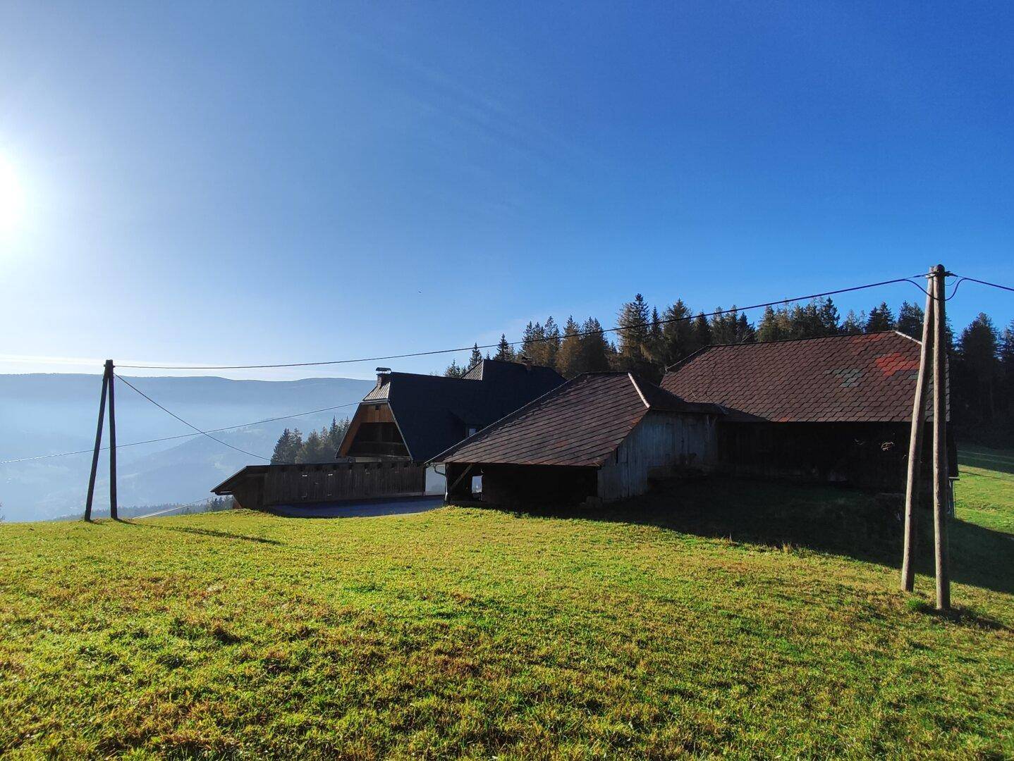 Weitläufige grüne Landschaft mit traditionellen Gebäuden und bewaldeten Hügeln unter strahlendem Himmel.