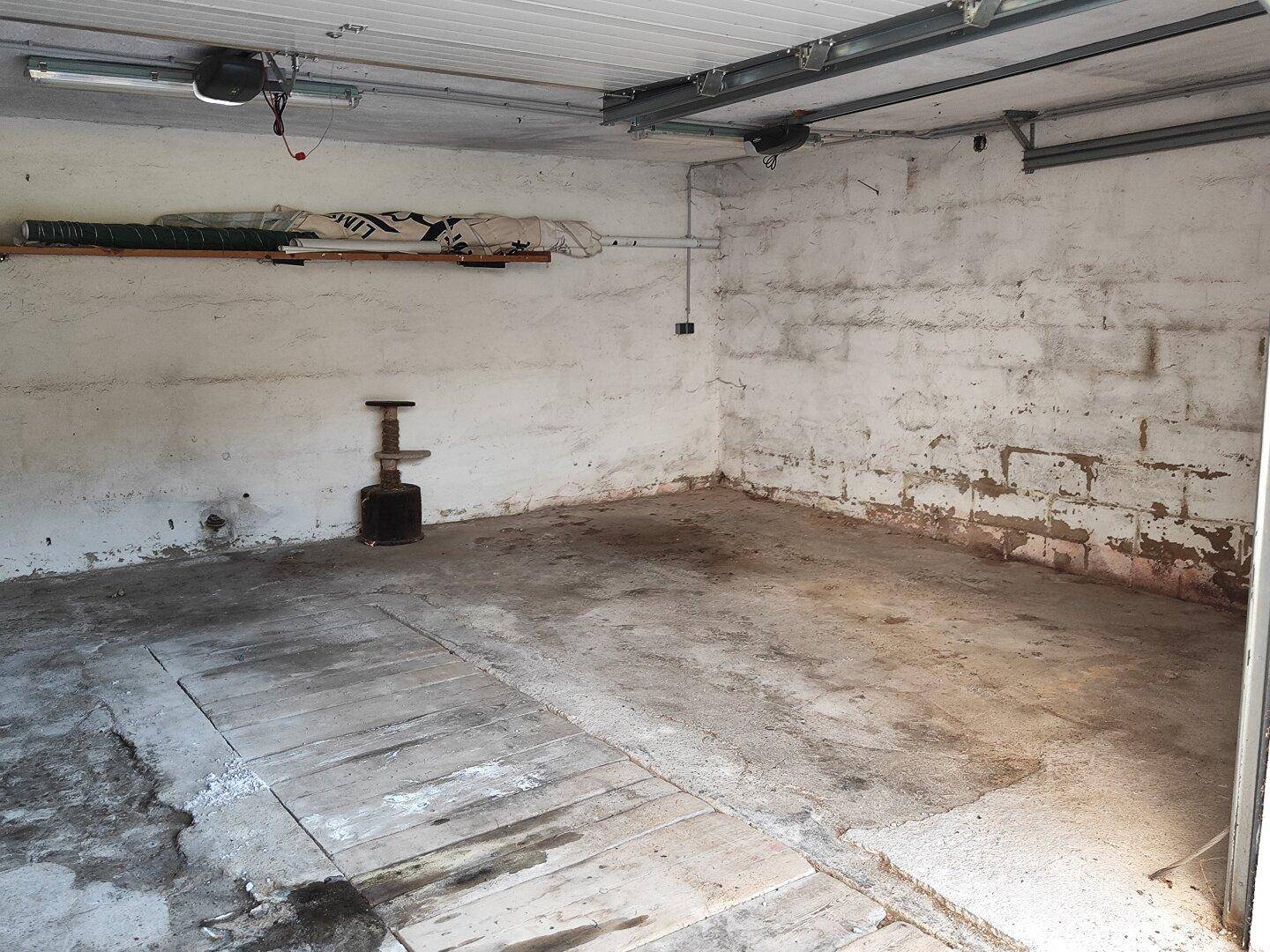 Innenansicht einer Garage mit Betonboden, abblätternder Farbe an den Wänden und Deckenmechanismen.