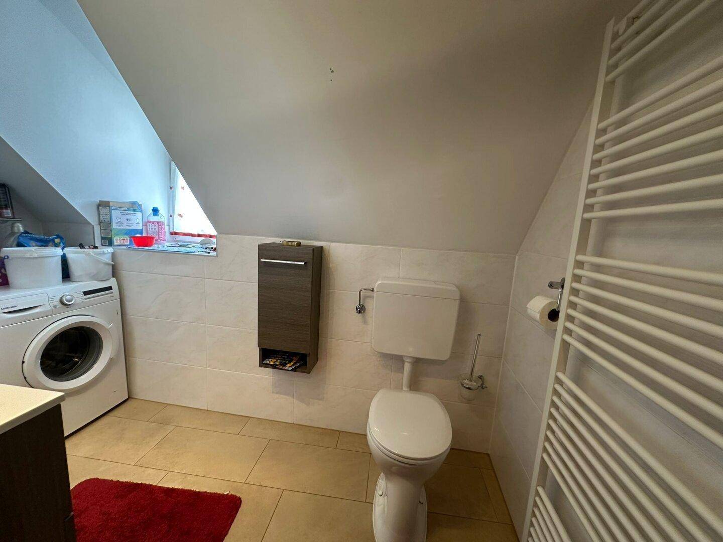 Badezimmer im Dachgeschoss mit Toilette, Waschmaschine und beheiztem Handtuchhalter.
