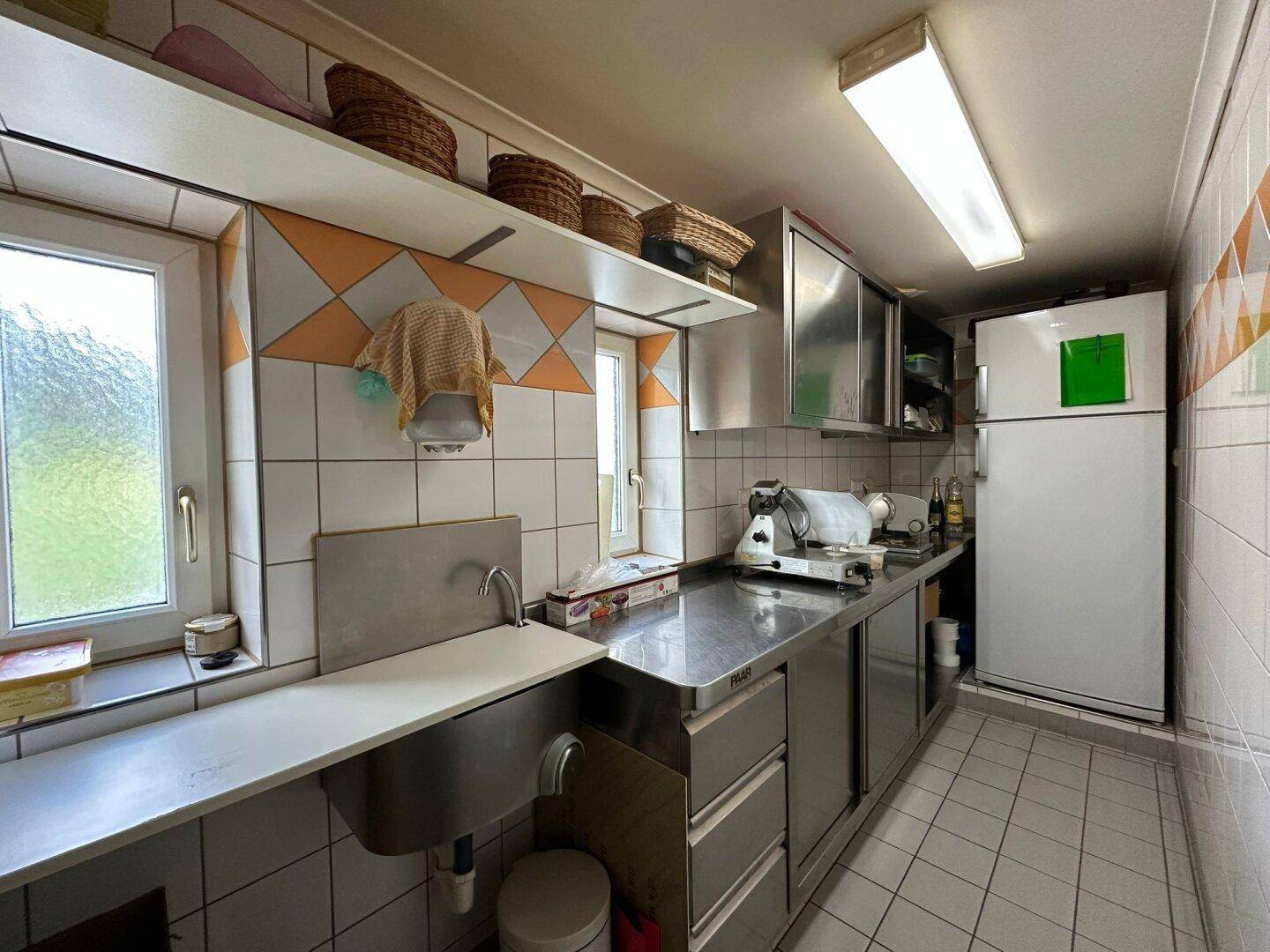 Funktionale Küche im Gastronomie-Stil mit Edelstahlflächen, Fliesenwänden und großem Kühlschrank.