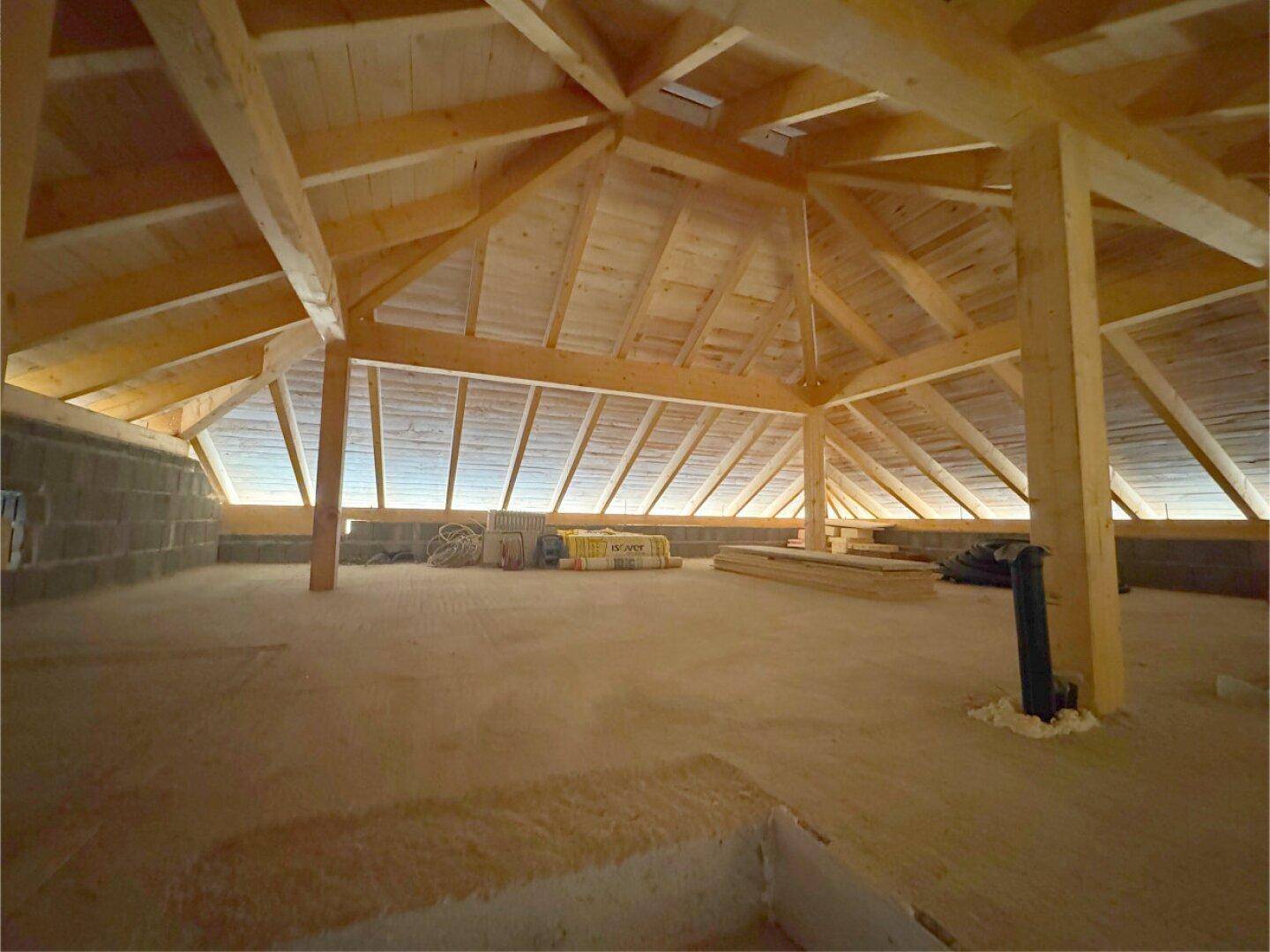 Geräumiger Dachboden im Rohbau mit sichtbarer Holzkonstruktion und Dachfenstern.