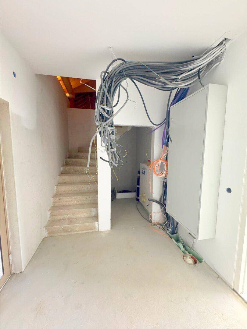 Eingangsbereich im Rohbau mit Treppe und sichtbaren Elektroinstallationen und Kabeln.