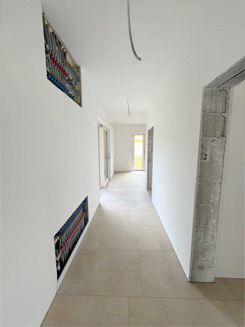 Heller Flur mit Fliesenboden und sichtbaren Installationen für die Fußbodenheizung.