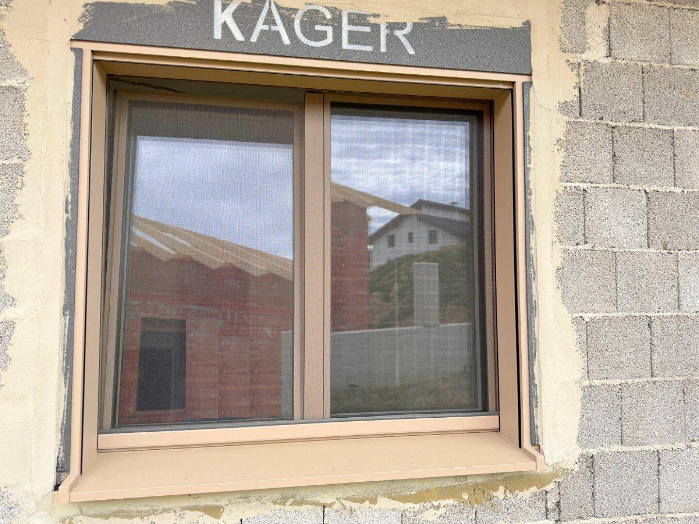 Neues Fenster mit beigem Rahmen und Fliegengitter, eingebaut in die Rohbauwand.