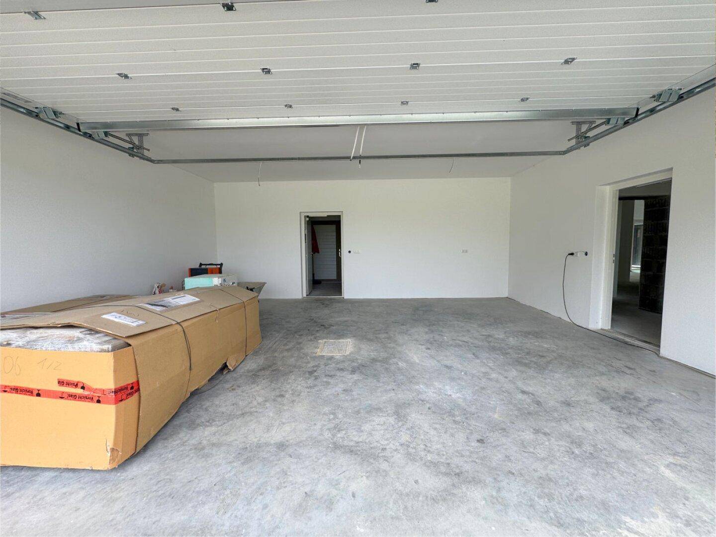Geräumige Garage im Rohbau mit Betonboden und Zugang zu weiteren Räumen.
