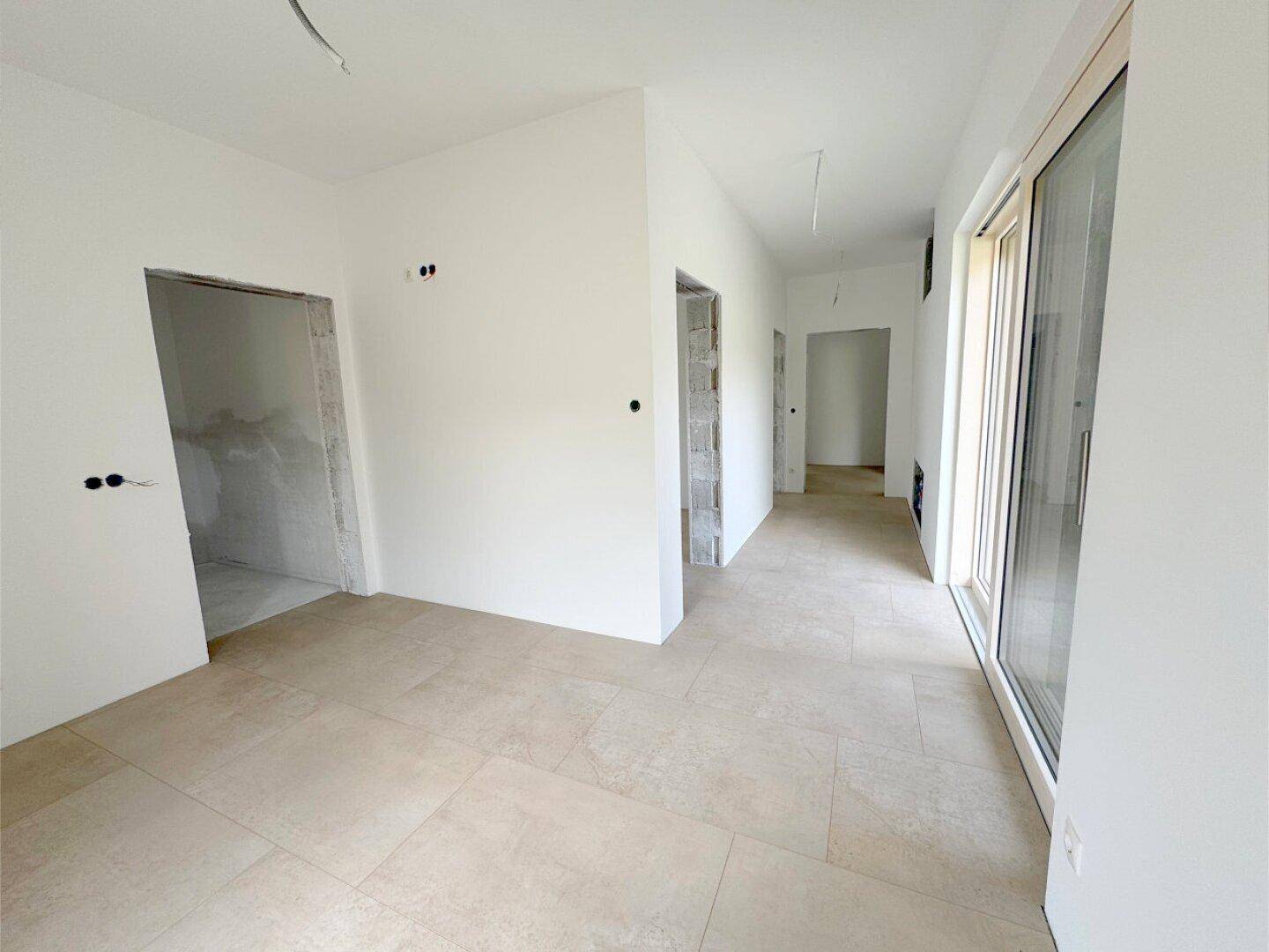 Geräumiger Flur mit Fliesenboden und Zugang zu mehreren Zimmern, noch im Rohbau.