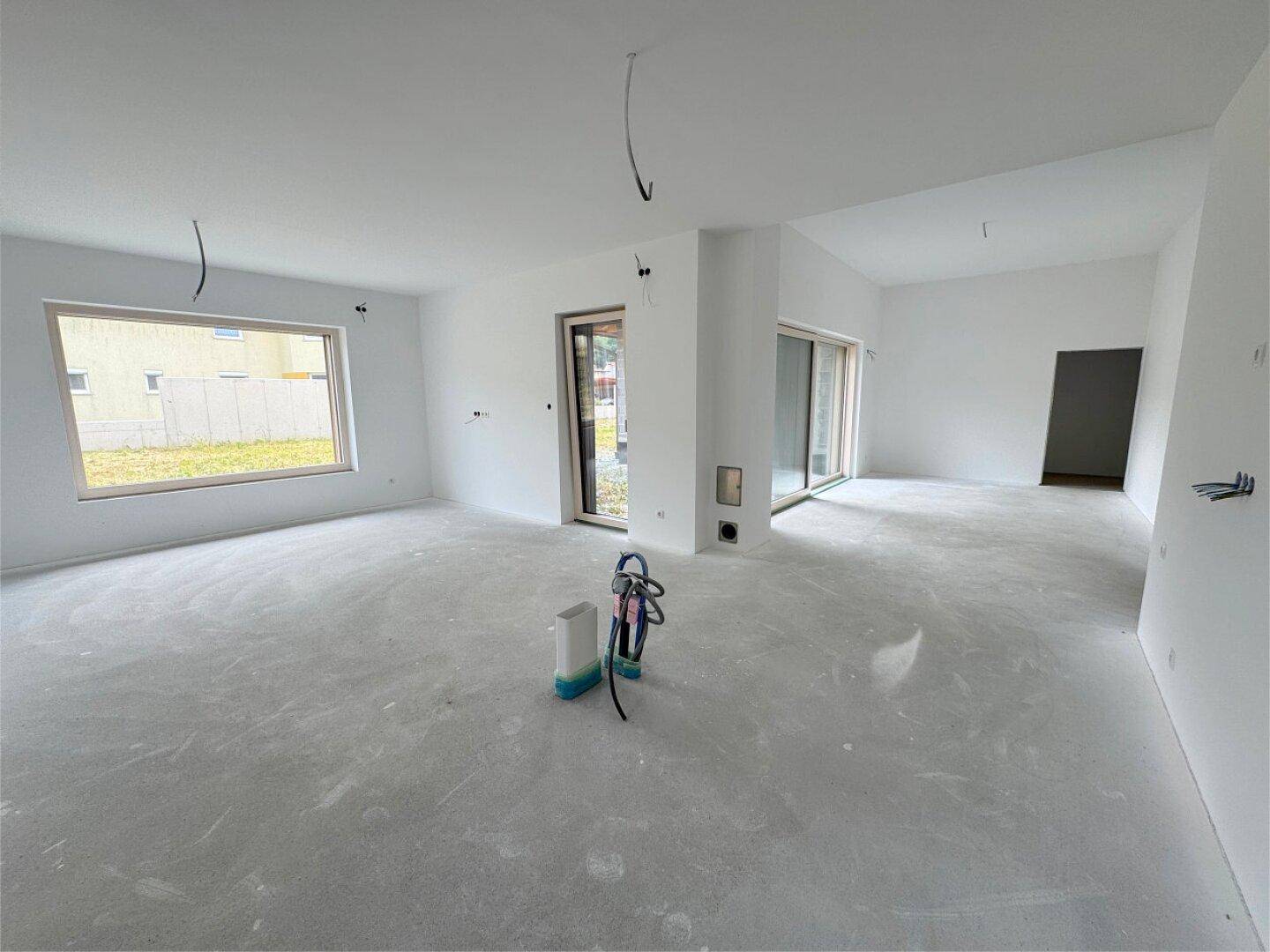 Geräumiges, helles Wohnzimmer im Rohbau mit großen Fenstern und Schiebetüren zum Garten.
