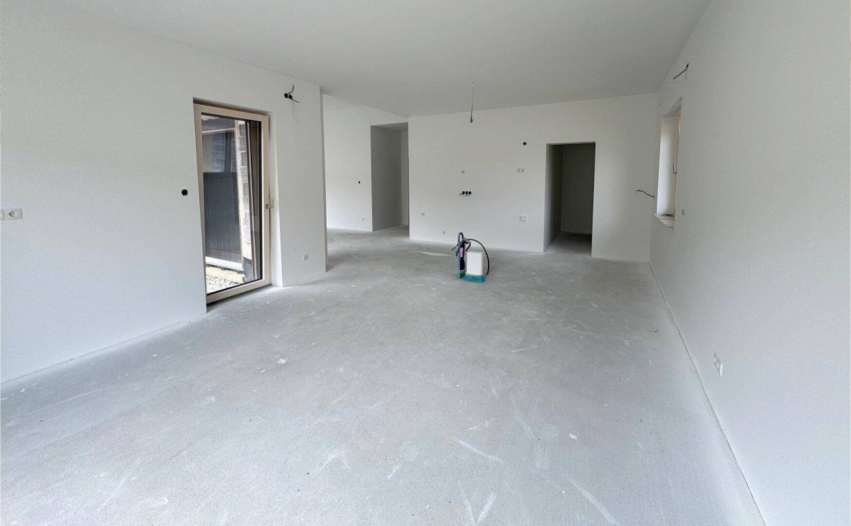 Heller Wohnbereich im Rohbau mit vorbereiteten Anschlüssen und Blick auf den Außenbereich.