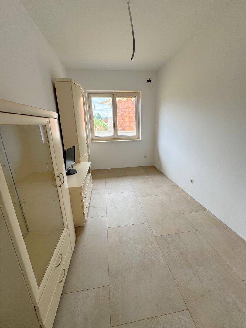 Schlafzimmer mit hellen Fliesen und einem Fenster, teilweise möbliert mit einem Schrank.