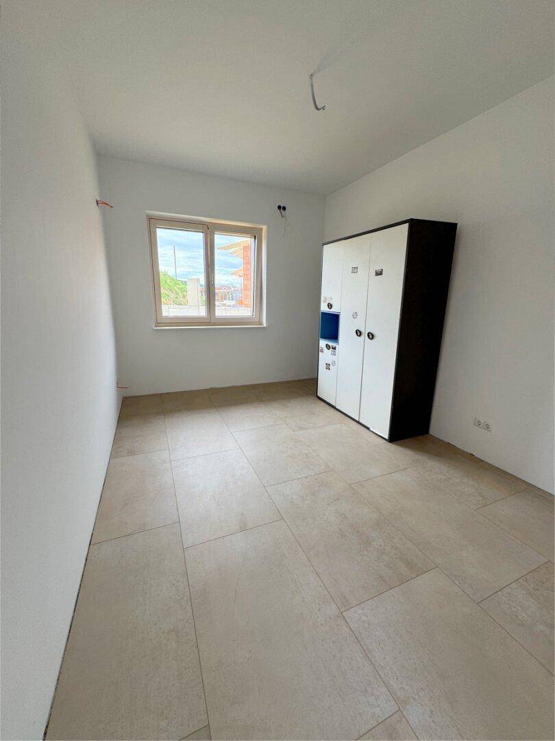 Schlafzimmer mit hellen Fliesen und einem Fenster, ausgestattet mit einem modernen Kleiderschrank.