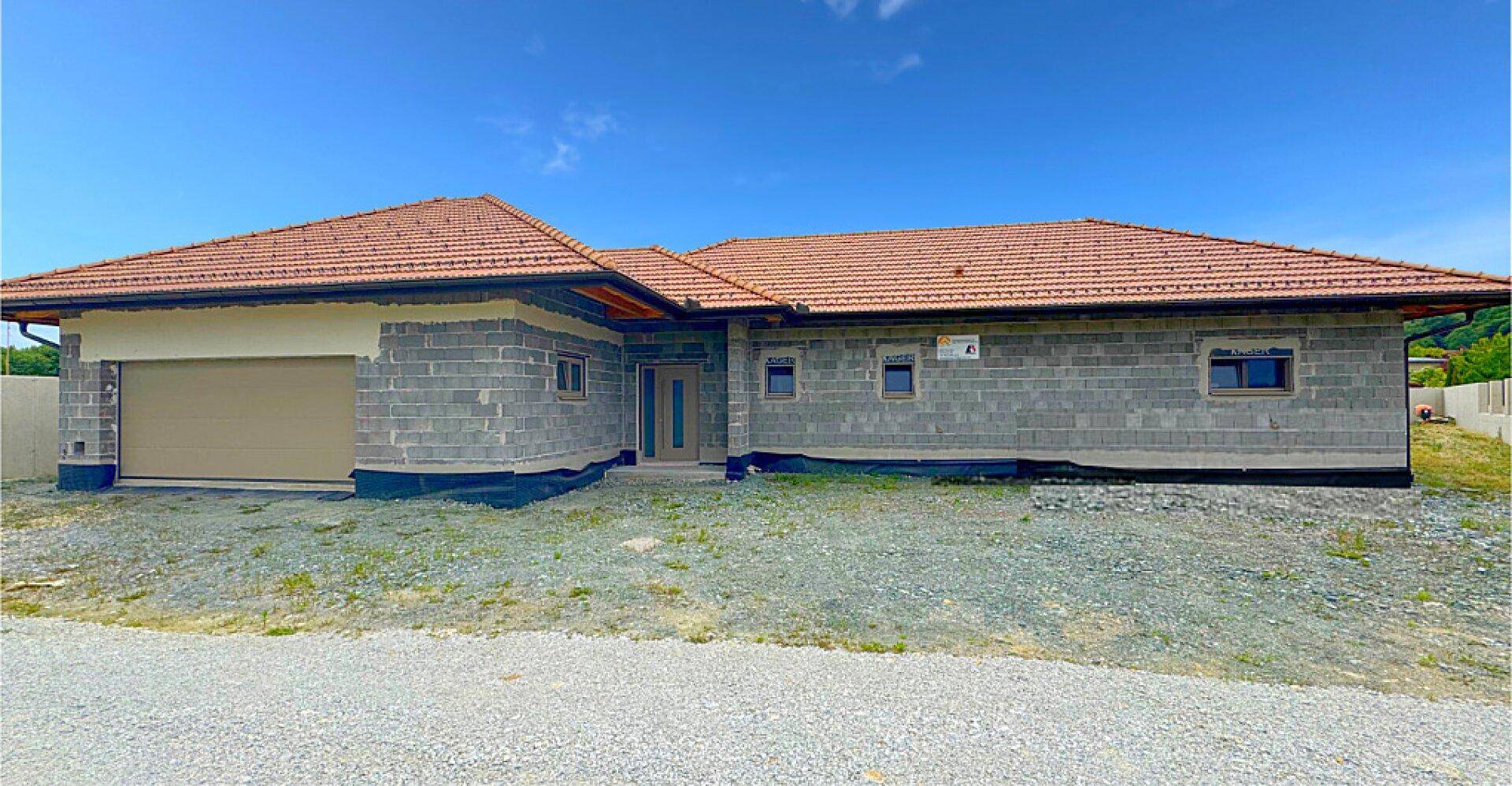 Seitenansicht eines neuen Einfamilienhauses mit Garage und Ziegeldach in ländlicher Umgebung.